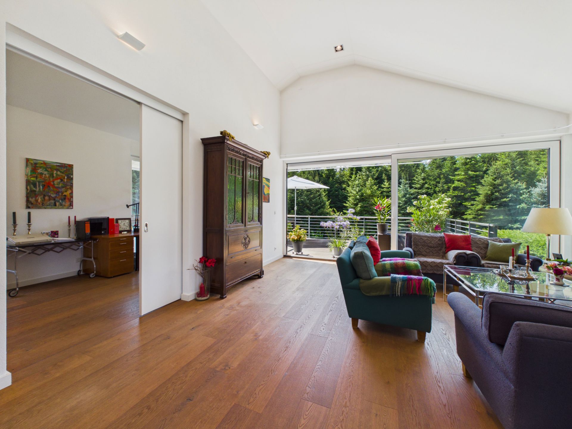 Helles Wohnzimmer mit Holzboden, großen Fenstern, Sofa und Zugang zur Terrasse mit Blick ins Grüne.