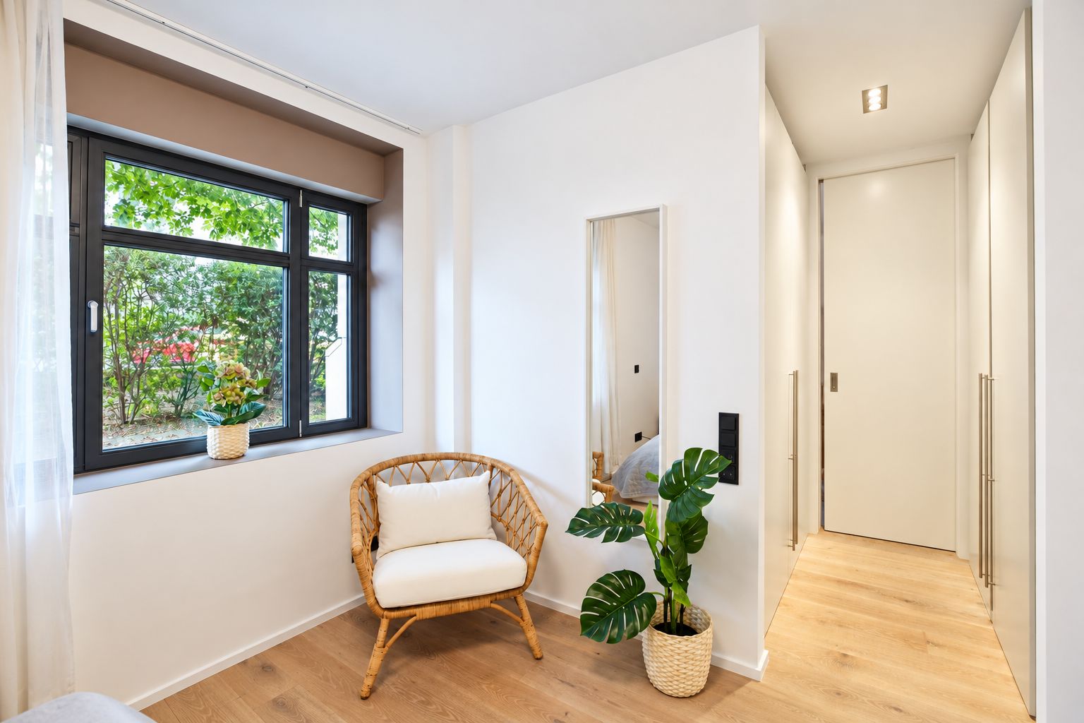 Helles Zimmer mit Sessel, großem Fenster, Spiegel und Zimmerpflanze auf Holzfußboden.