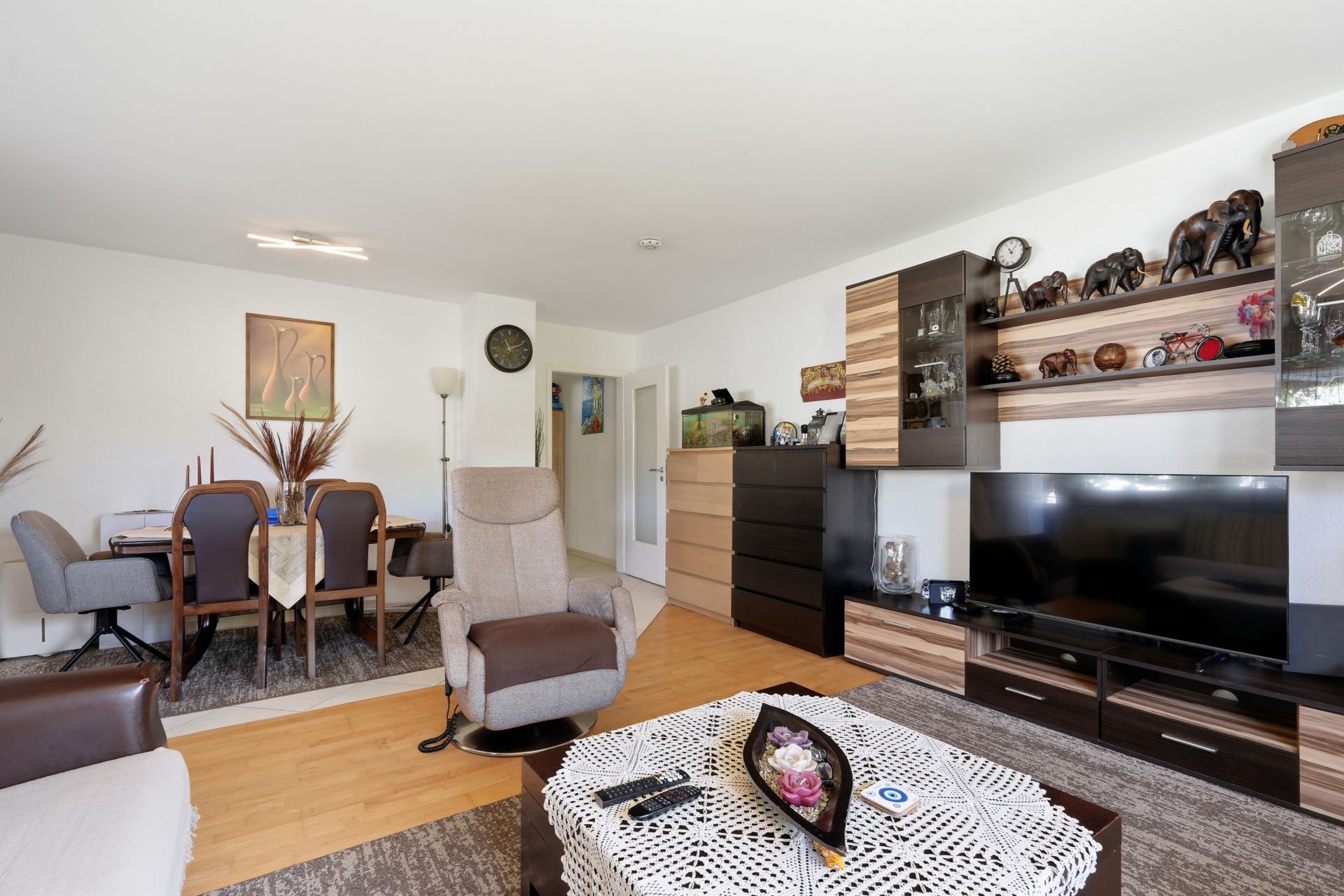 Wohnzimmer mit TV, Schrankwand, Esstisch, Sessel und dekoriertem Couchtisch.