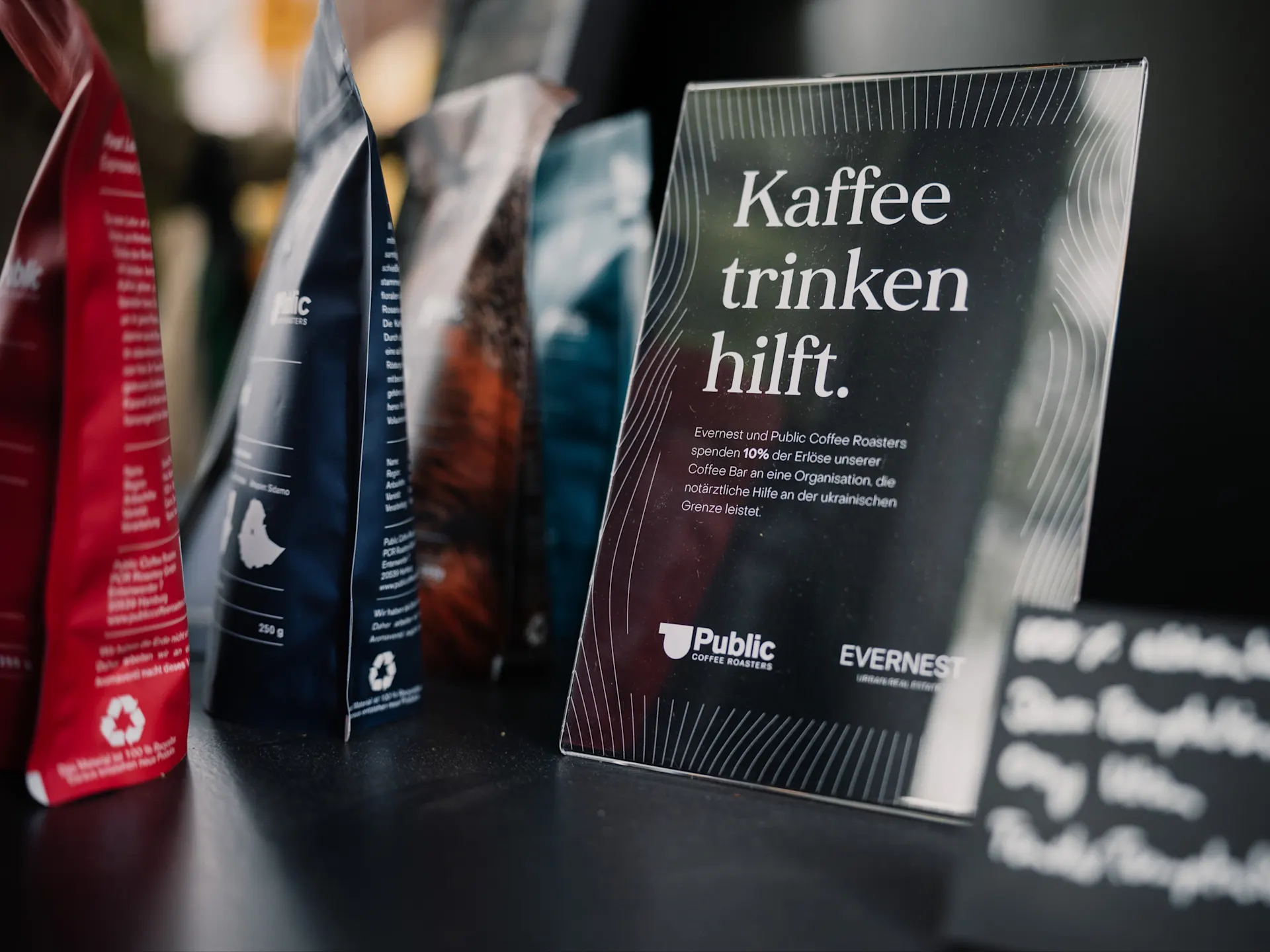Kaffeeverpackungen und ein Aufsteller mit dem Text 'Kaffee trinken hilft.' auf einem Tisch.