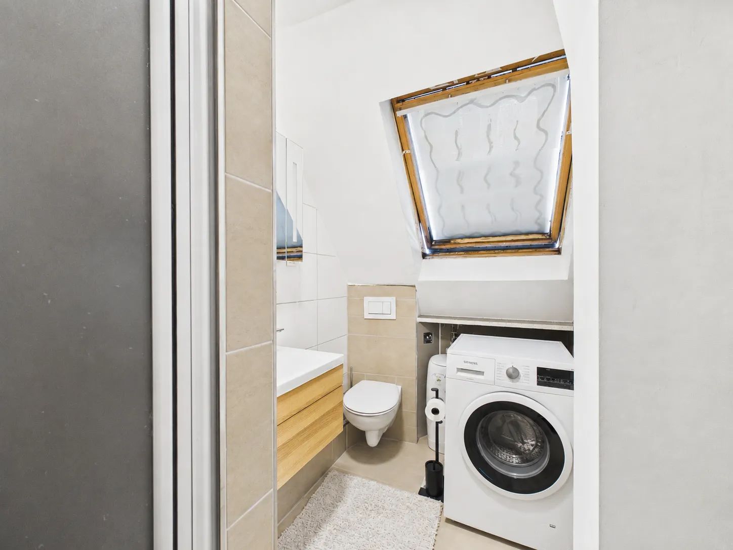 Kleines Badezimmer mit Waschmaschine, Toilette, Waschbecken und Dachfenster.