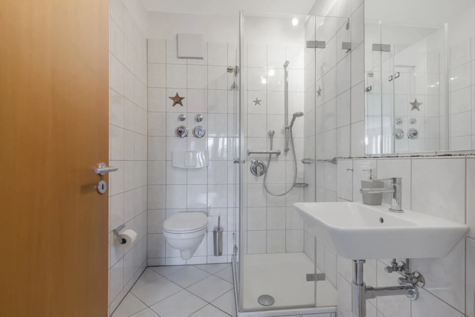 Modernes Badezimmer mit Dusche, Waschbecken und Wand-WC, weiße Fliesen an Wänden und Boden.