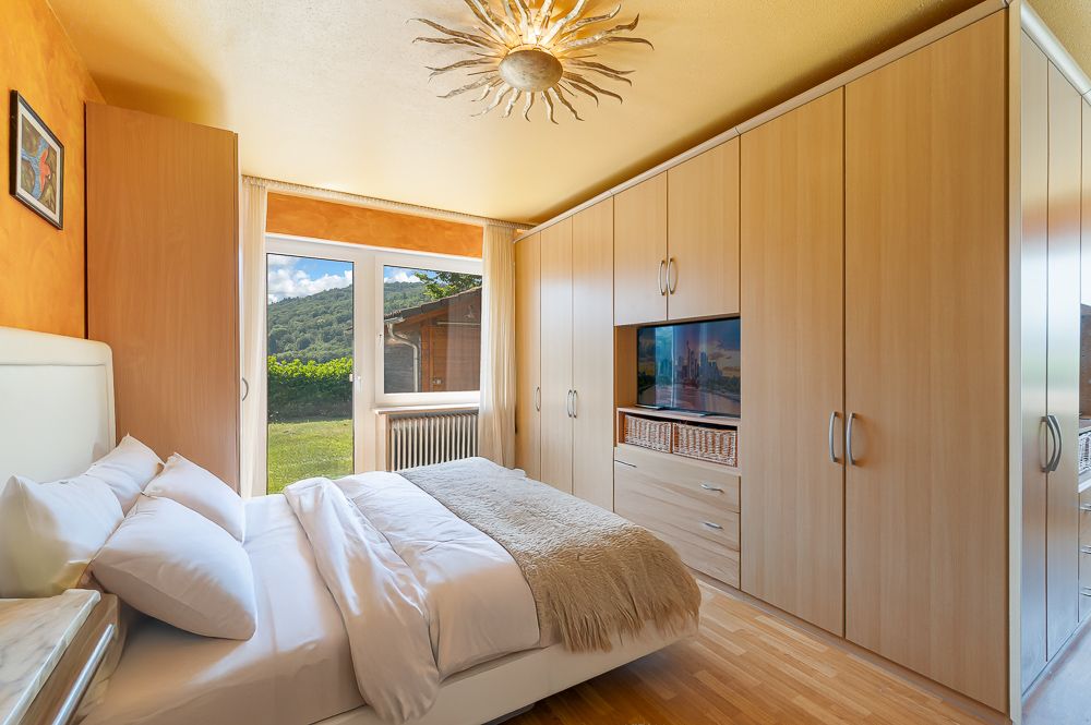 Helles Schlafzimmer mit großem Bett, Einbauschrank und Fenster mit Blick ins Grüne.
