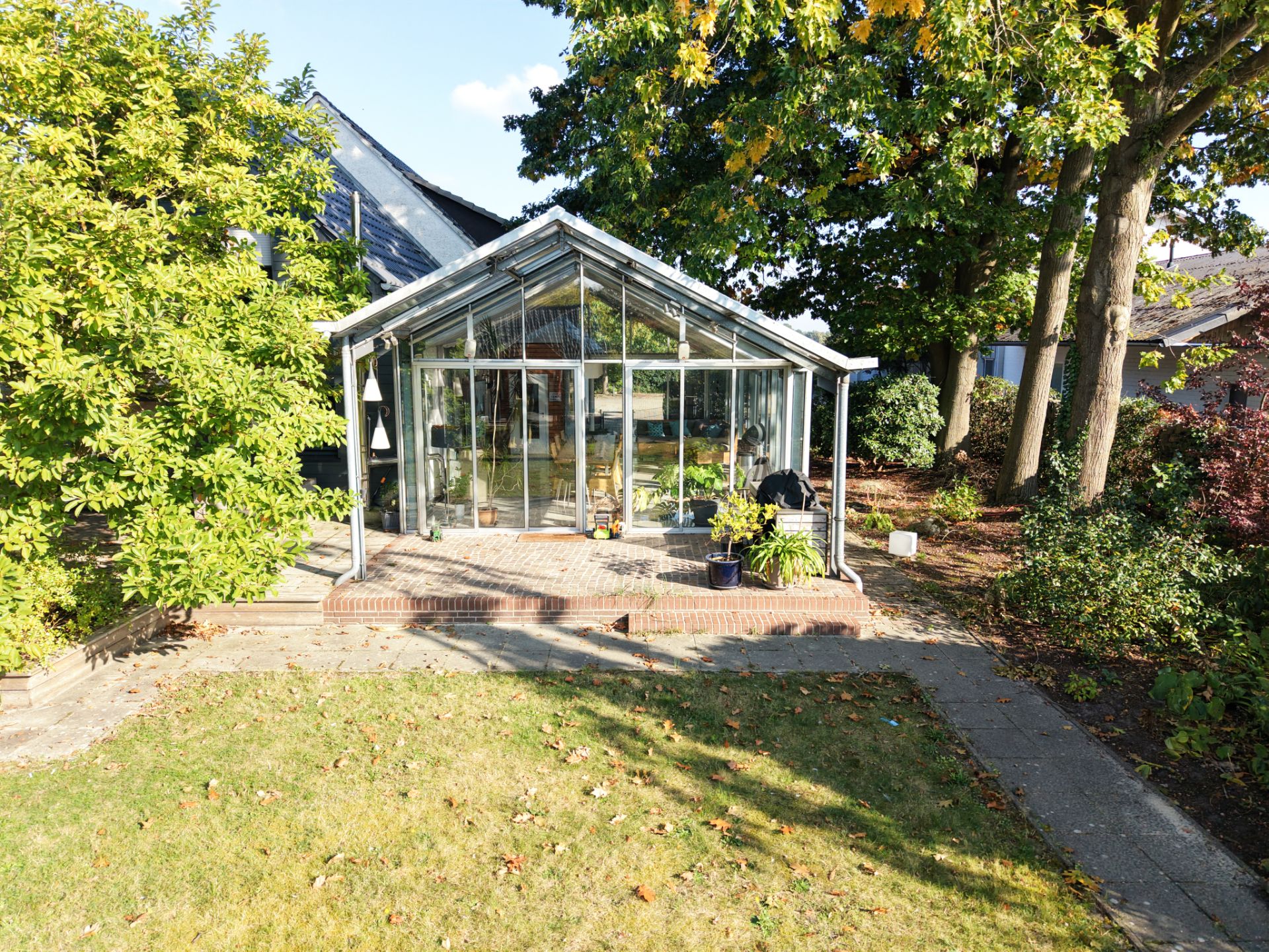 Glas-Wintergarten an einem Wohnhaus, umgeben von Garten und Bäumen.
