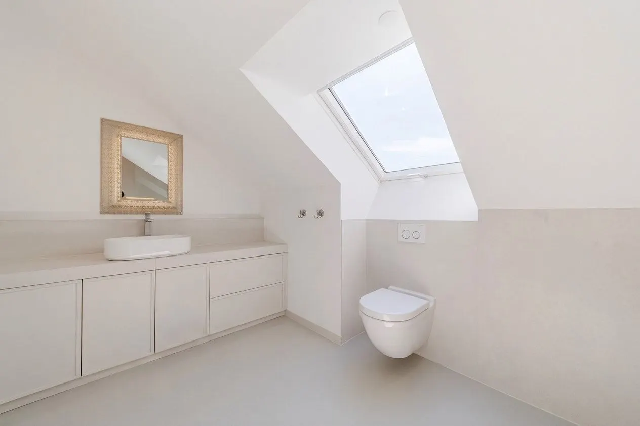 Helles Badezimmer mit Waschbecken, Spiegel, Hängetoilette und Dachfenster.