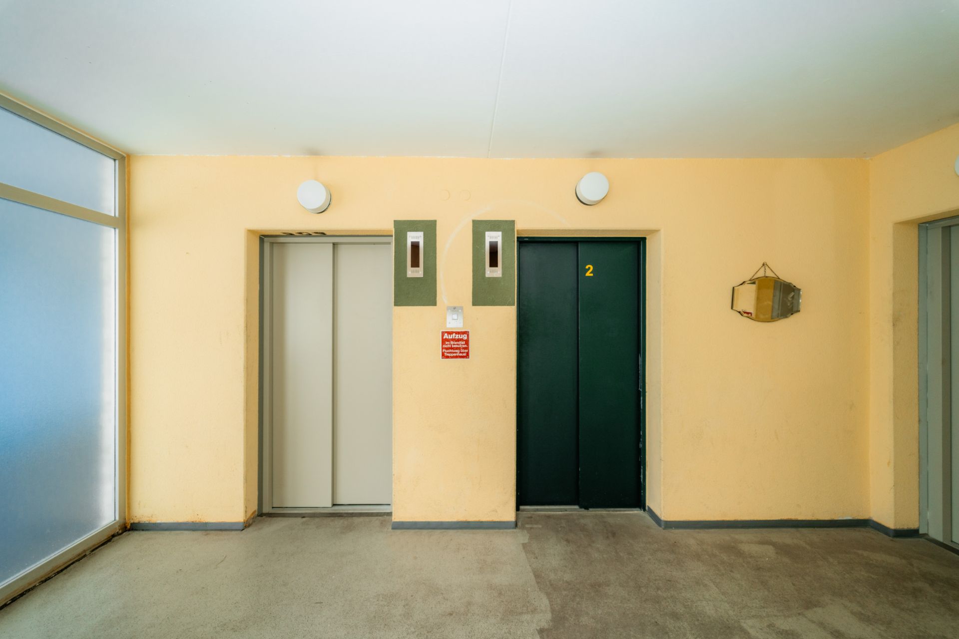 Flur mit zwei Aufzugtüren und einem Spiegel an der Wand.
