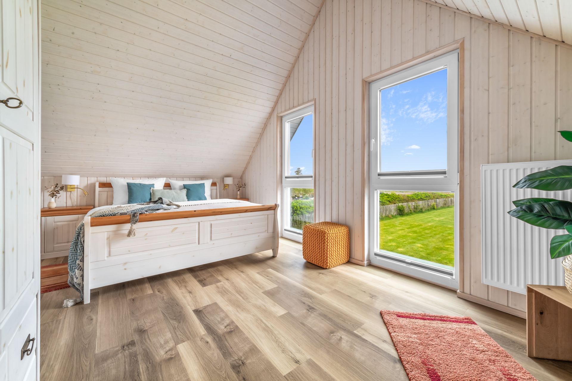 Helles Schlafzimmer mit Holzdecke, großem Bett und zwei Fenstern mit Blick auf den Garten.