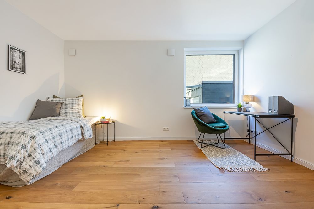 Helles Schlafzimmer mit Einzelbett, Nachttisch, Schreibtisch und Stuhl, Holzfußboden.