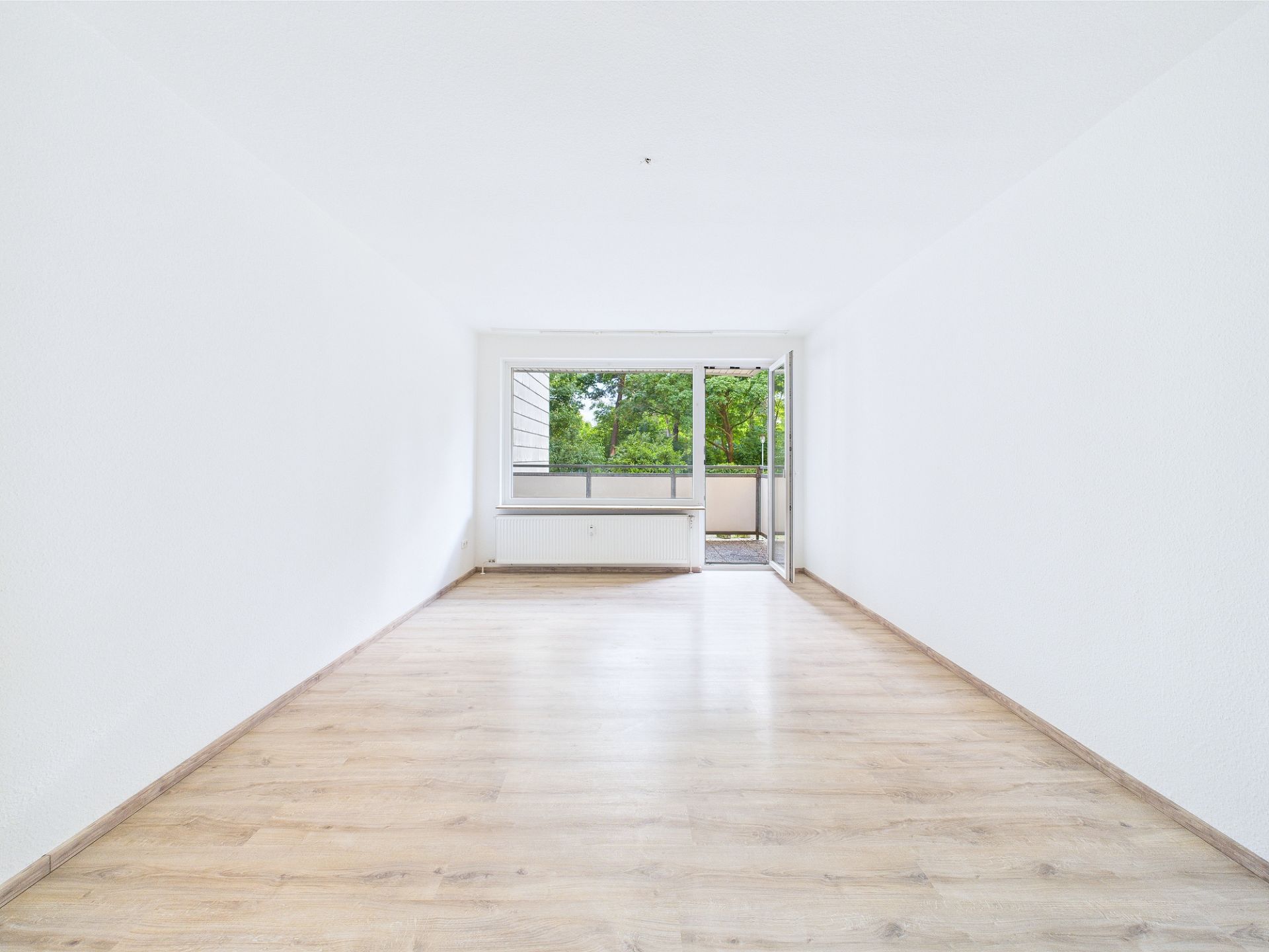 Leerer, heller Raum mit Holzfußboden und großem Fenster zur Terrasse.