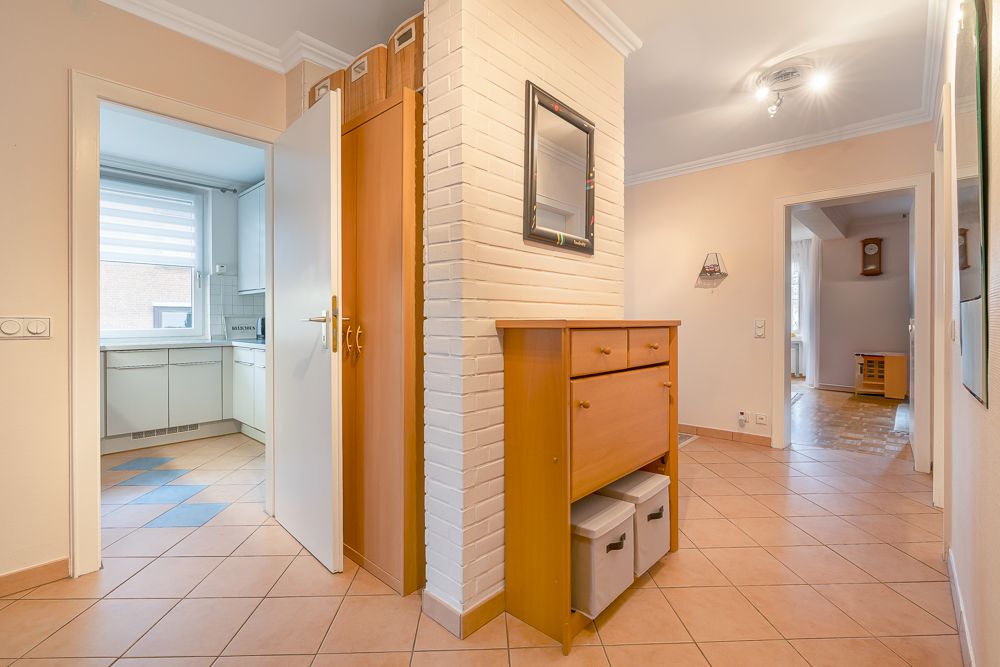 Flur mit Fliesenboden, Kommode, Spiegel und Aussicht in die Küche und ein weiteres Zimmer.