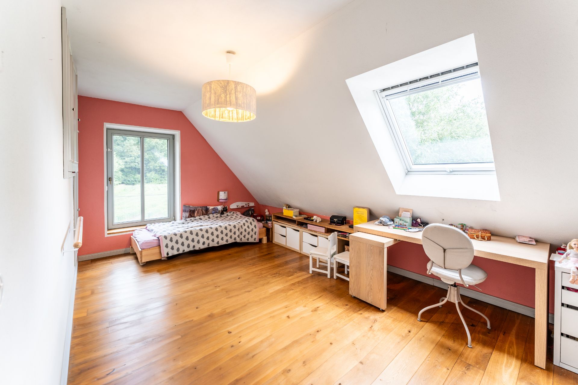 Helles Kinderzimmer mit Dachschräge, Einzelbett, Schreibtisch und großem Fenster.