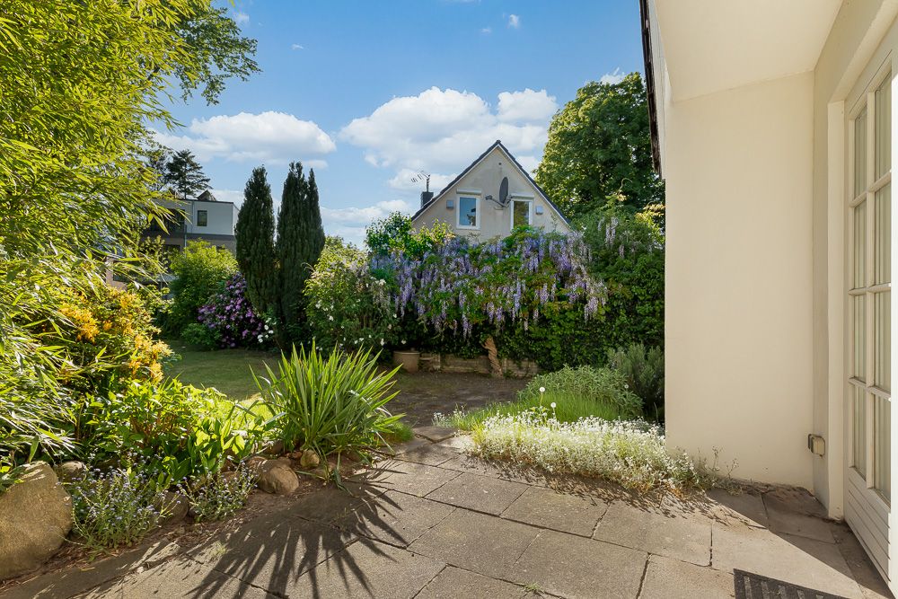 Blick von einer Terrasse auf einen Garten mit Blumen, Sträuchern und Rasen bei sonnigem Wetter.