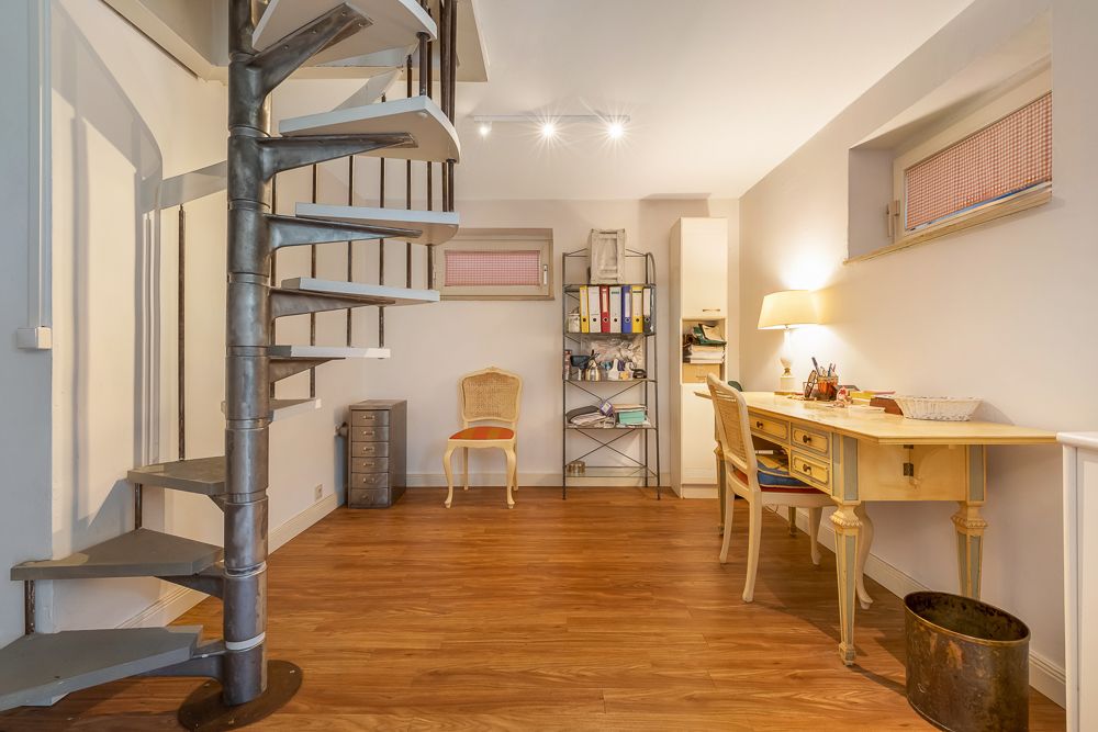 Helles Arbeitszimmer mit Wendeltreppe, Schreibtisch, Regal, Stuhl und Holzfußboden.
