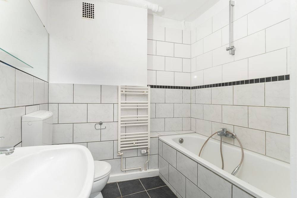 Weiß gefliestes Badezimmer mit Badewanne, Waschbecken, Toilette und Handtuchheizkörper.