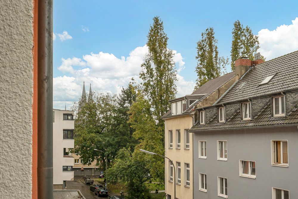Blick aus Fenster auf Wohnhäuser, Bäume und blauen Himmel mit Wolken.