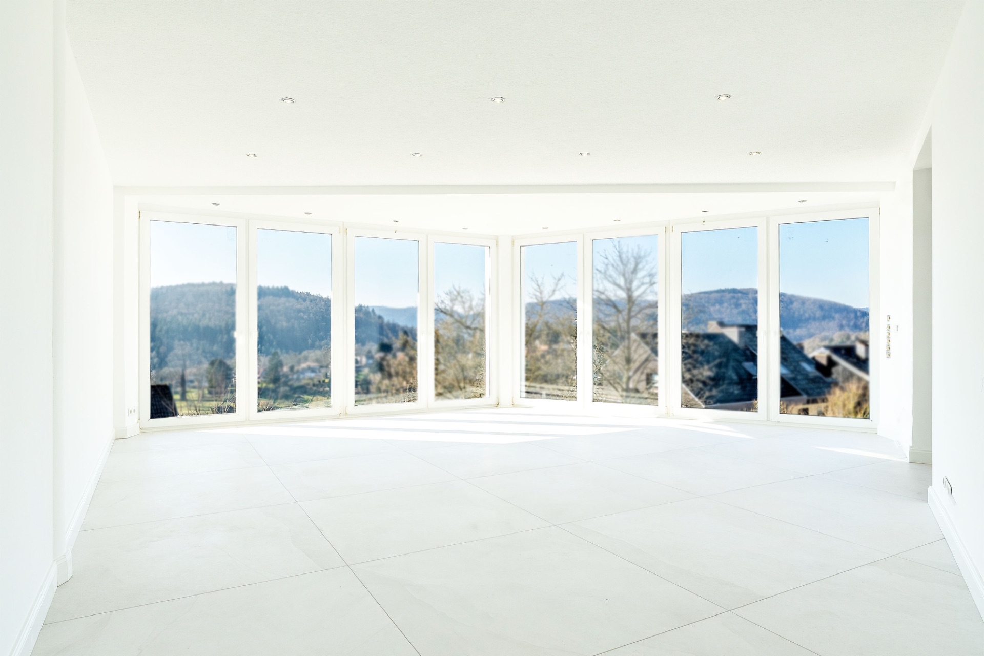 Heller, leerer Raum mit großen Fenstern und Blick auf Hügel und Bäume.