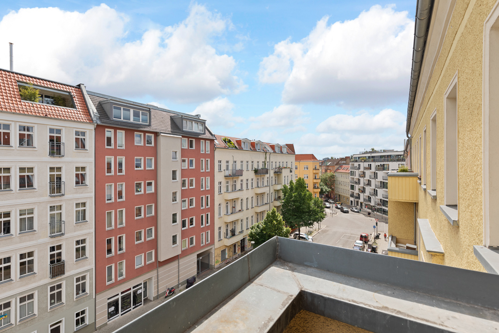 Blick von einem Balkon auf eine ruhige Wohnstraße mit mehrstöckigen Häusern und Bäumen.