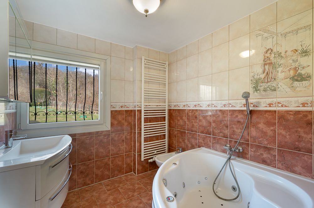Badezimmer mit Eckbadewanne, Waschbecken, Fenster und Handtuchheizkörper.