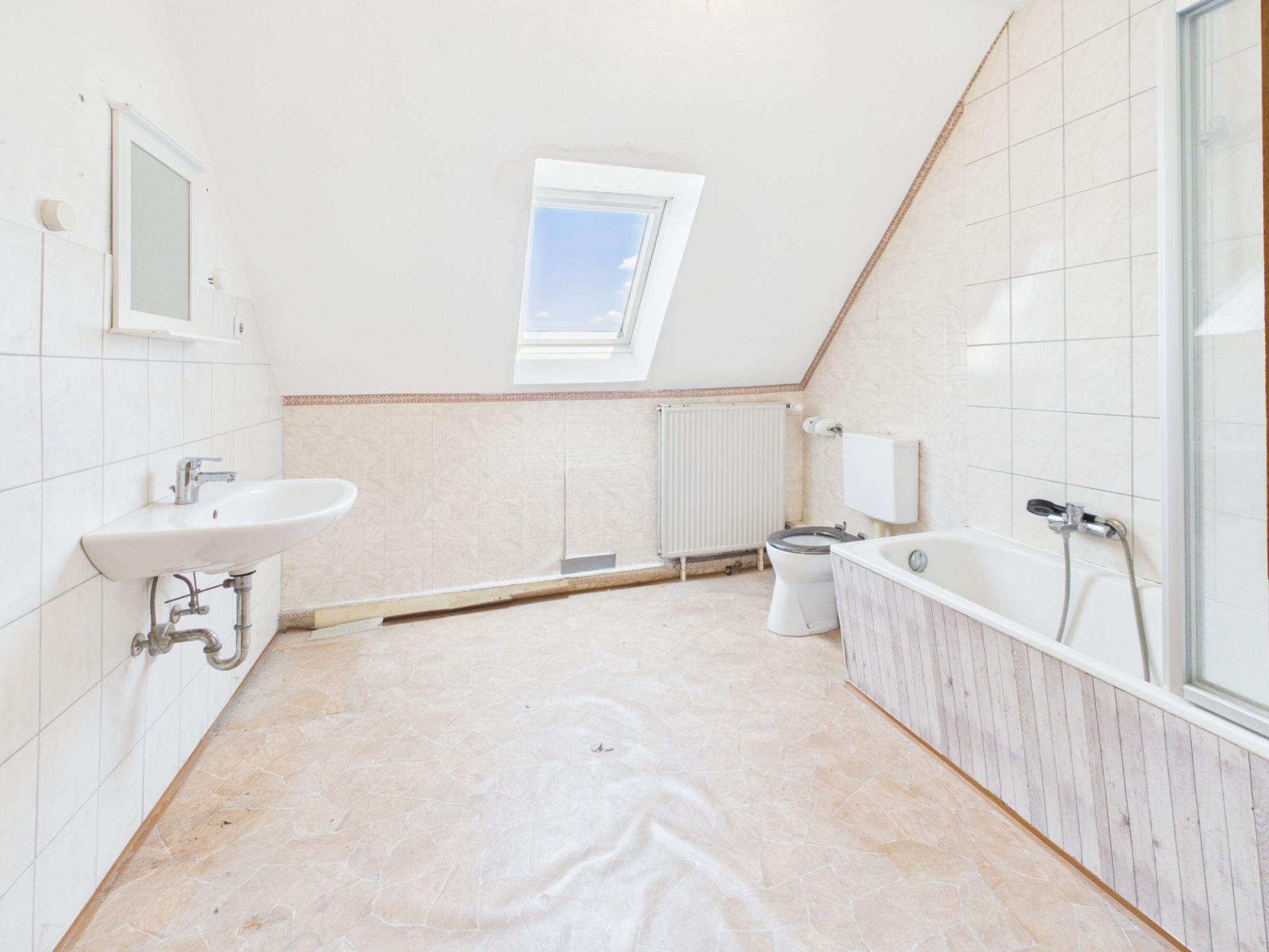 Helles Badezimmer mit Dachfenster, Badewanne, Waschbecken und Toilette.