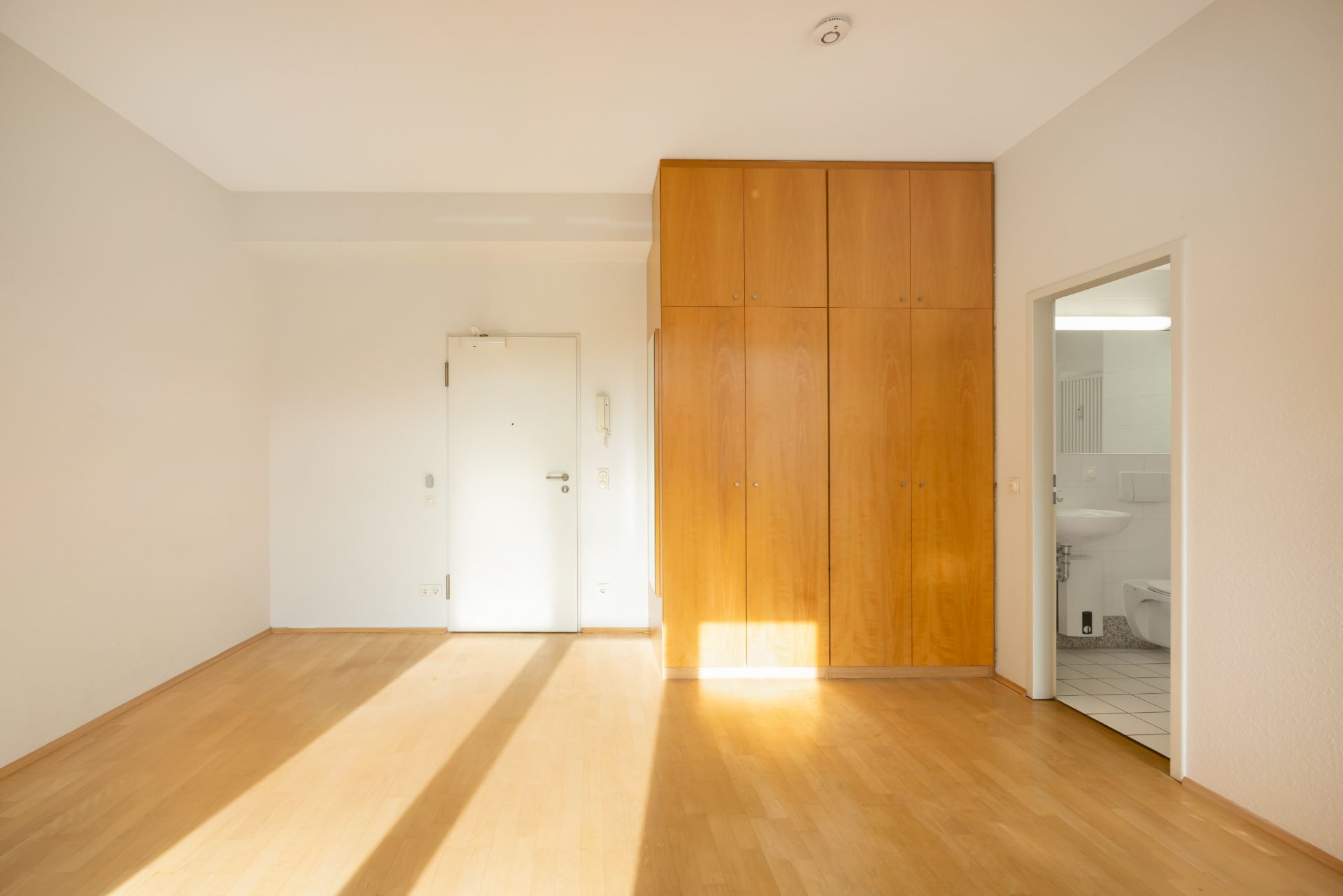 Heller Raum mit Holzboden, großem Einbauschrank und Blick ins Badezimmer.