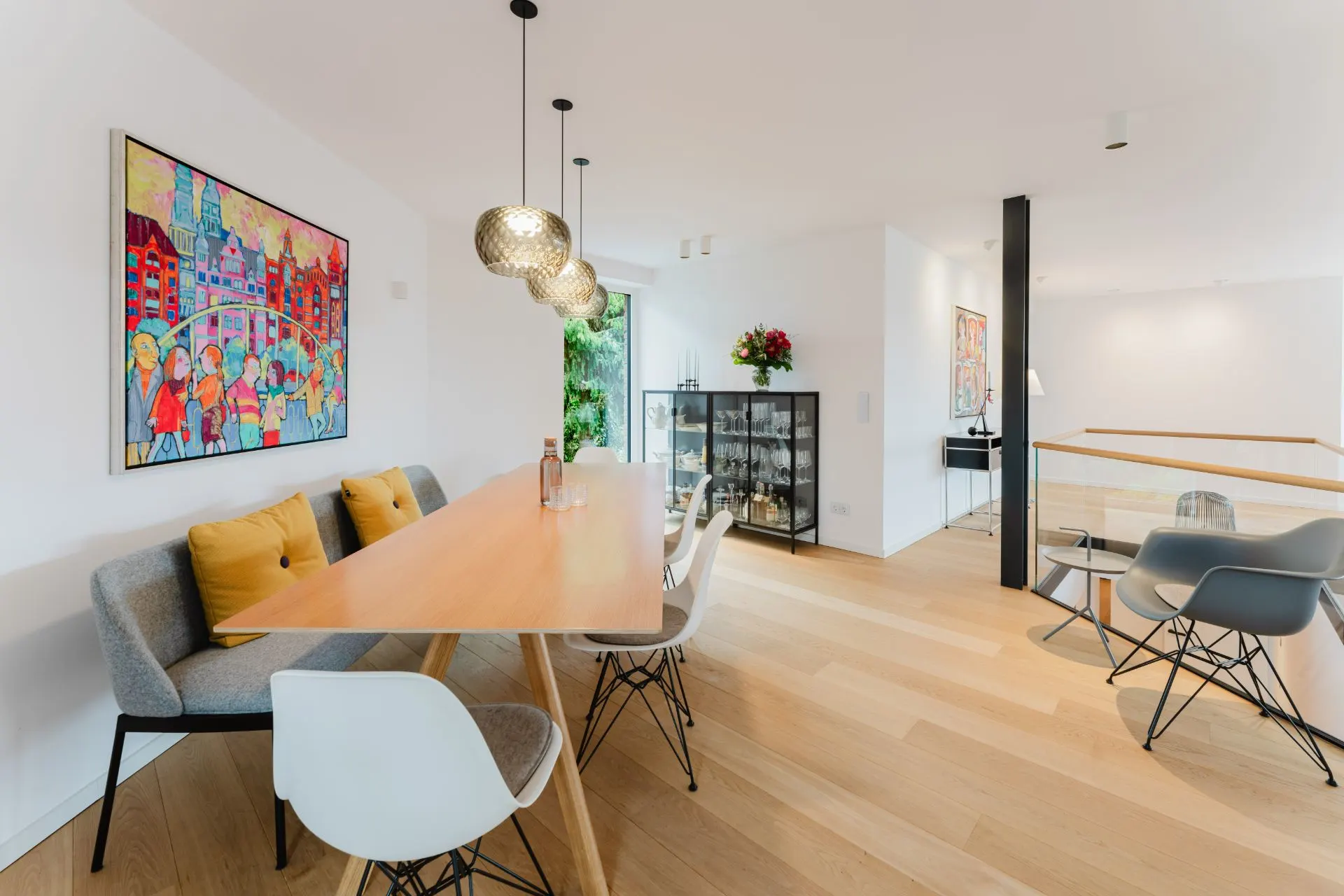 Modernes Esszimmer mit Holztisch, Stühlen, Wandbild und Glasvitrine in hellem Raum.