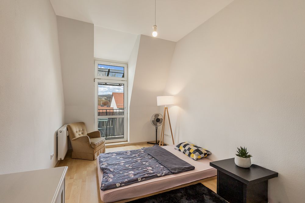 Helles Schlafzimmer mit Matratze am Boden, Sessel, Nachttisch und Stehlampe.