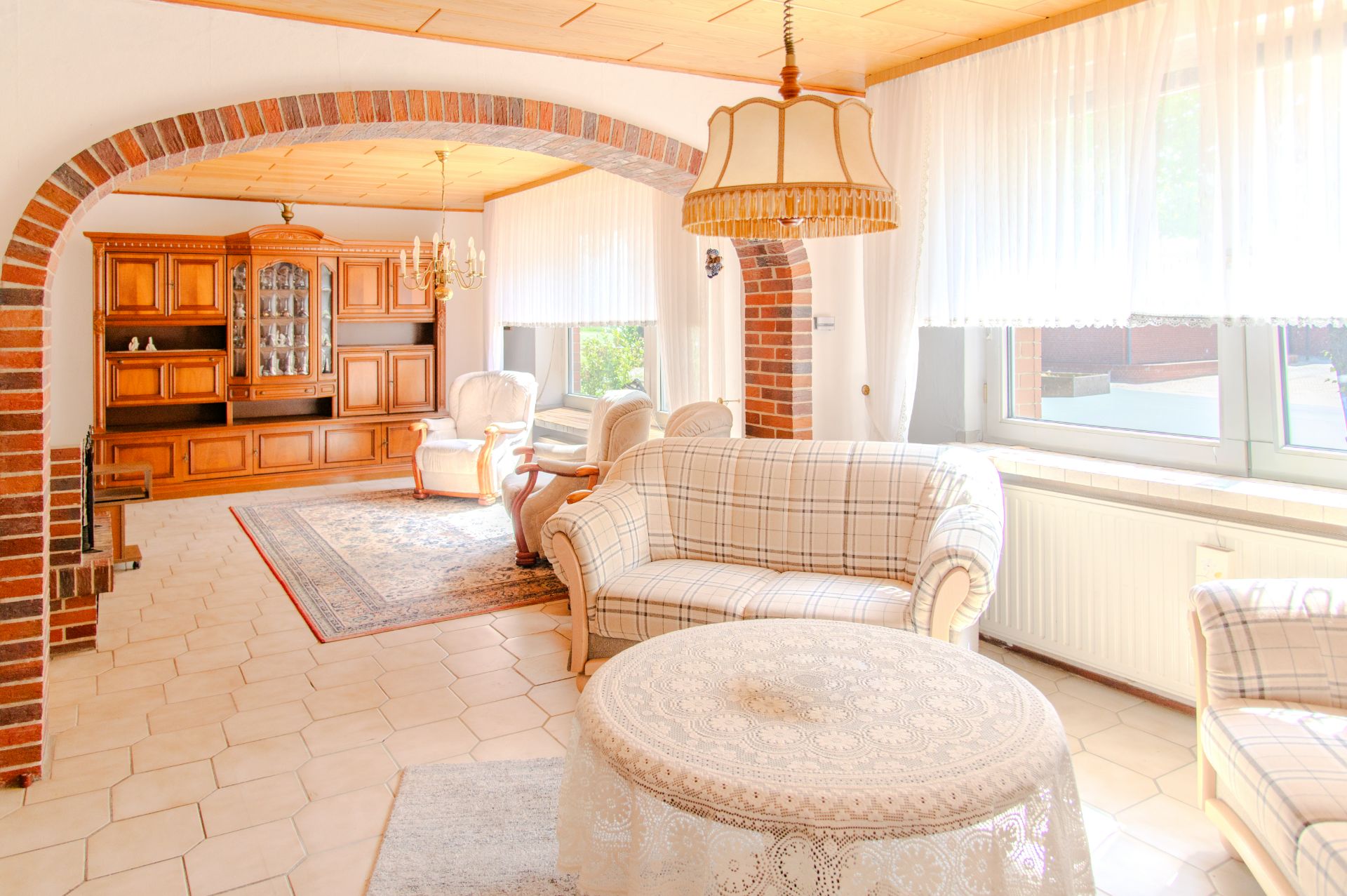 Helles Wohnzimmer mit karierten Sofas, Holzmöbeln, großen Fenstern und gemauerten Rundbögen.