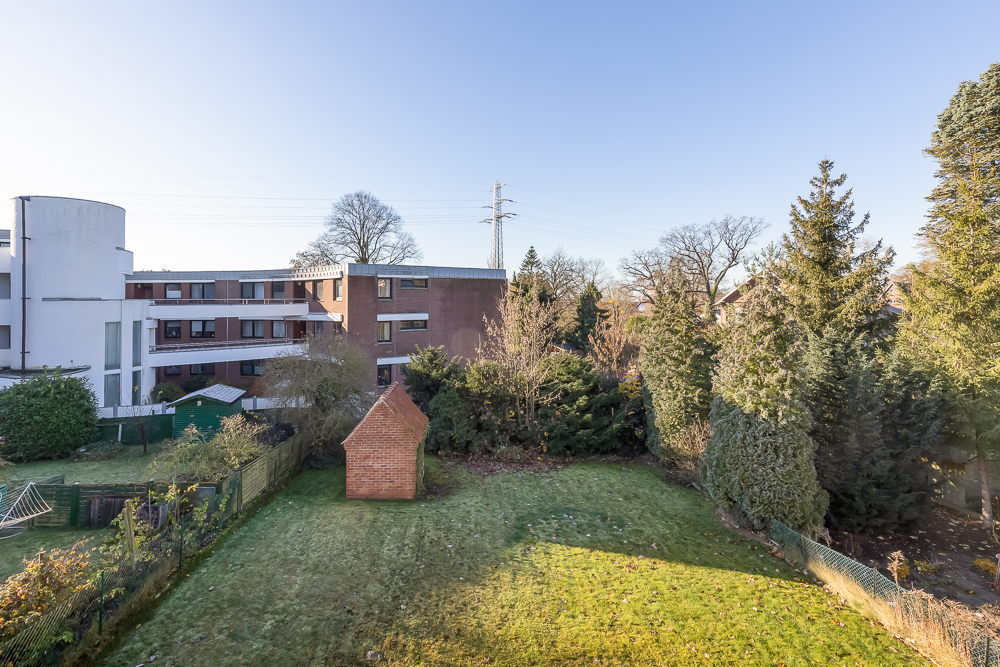 Blick auf einen Garten mit Rasen, Bäumen und einem kleinen roten Ziegelhaus.
