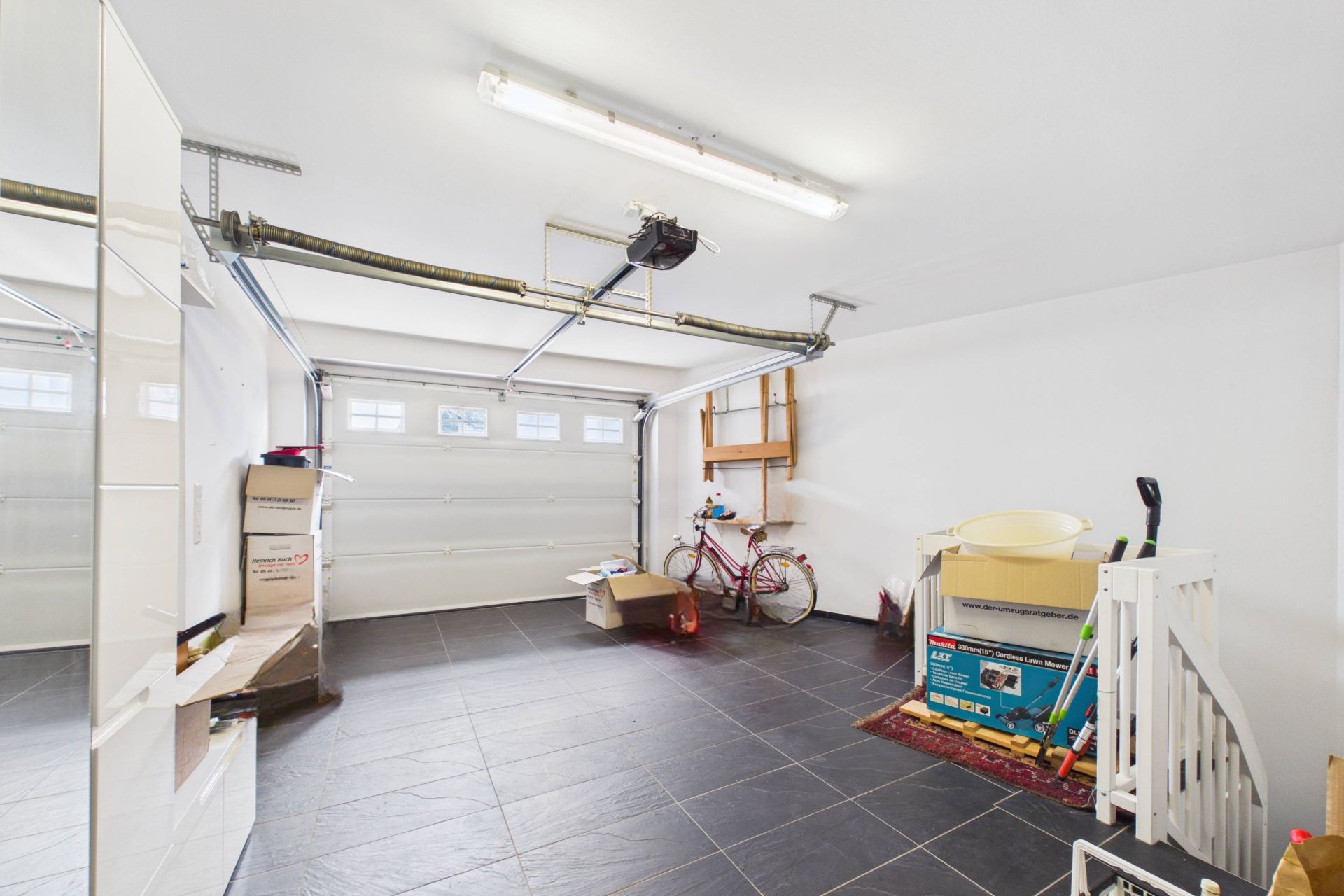 Geräumige Garage mit Fahrrad, Kartons, Regalen und Haushaltsgegenständen.