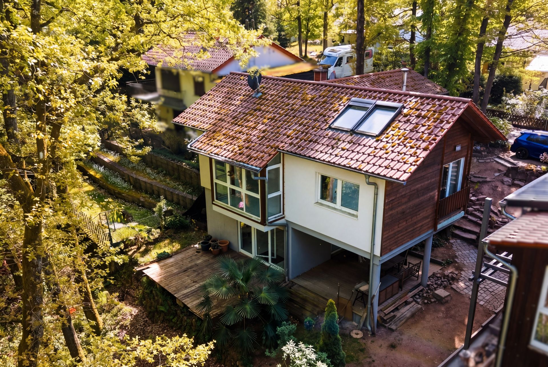 Modernes Wohnhaus mit rotem Ziegeldach und großer Holzterrasse im Grünen.