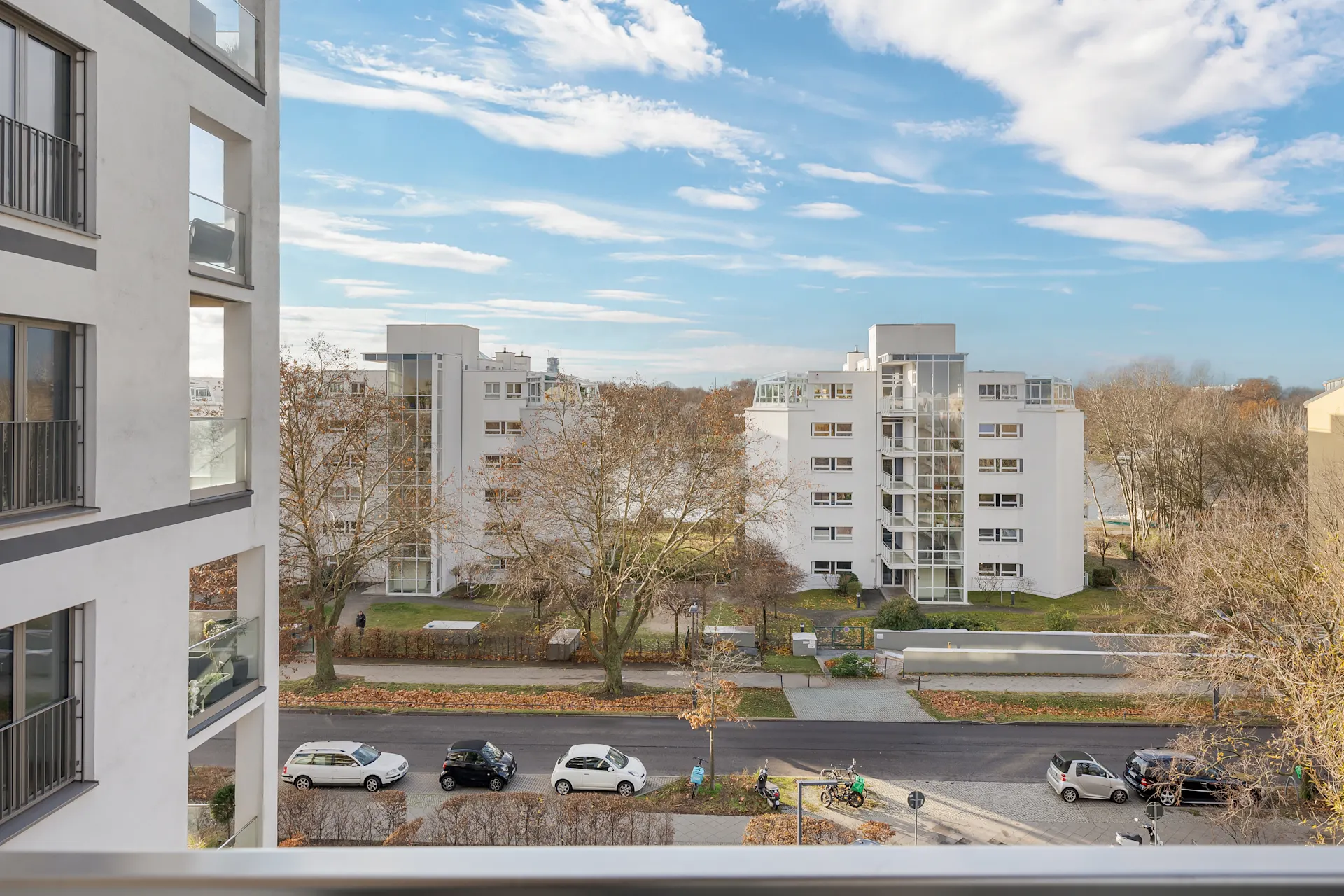 Aussicht auf moderne Wohngebäude mit Balkonen, Bäumen und geparkten Autos an einer Straße.