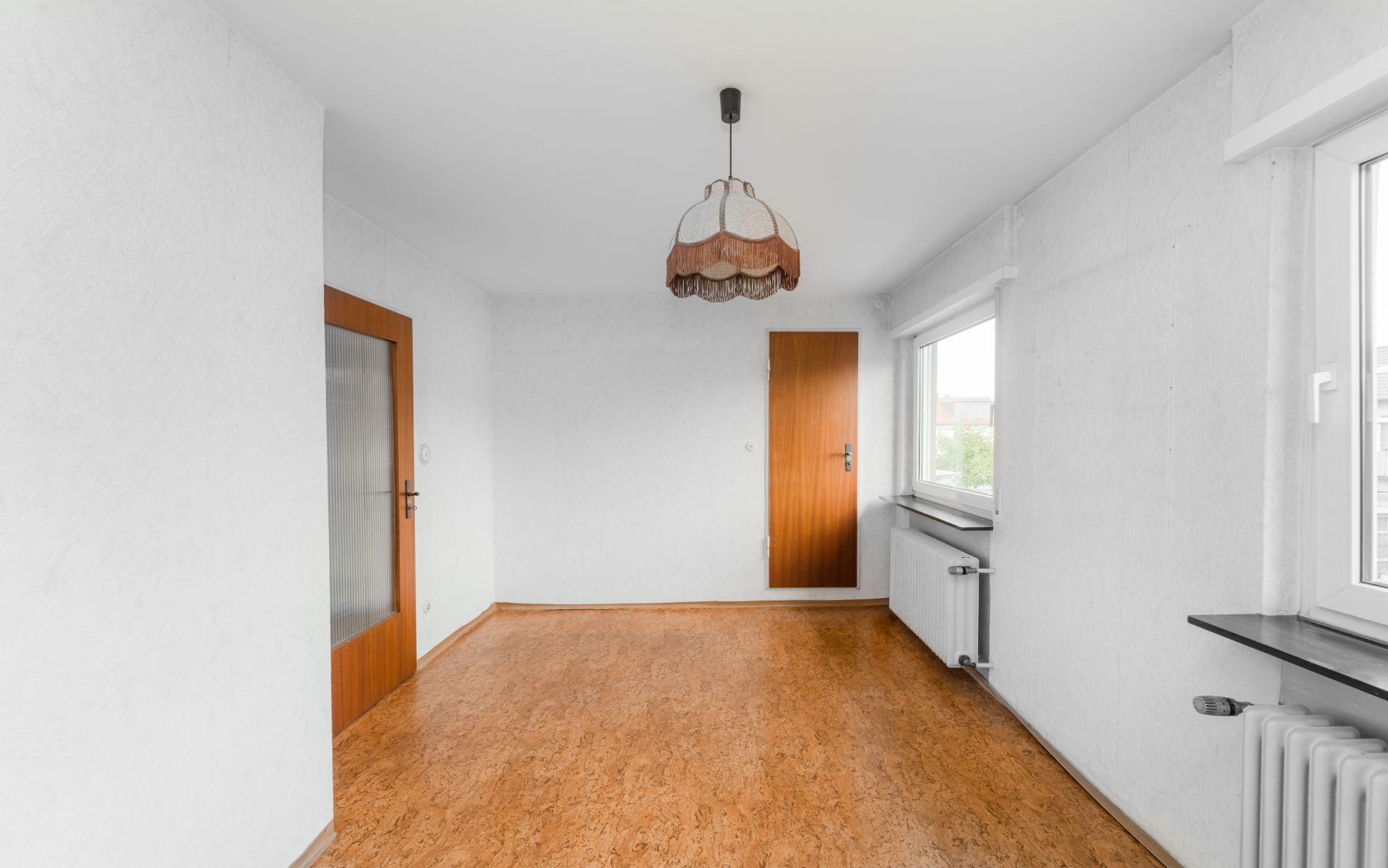 Leerer Raum mit Holztüren, Fenstern, weißer Wand und Deckenlampe.