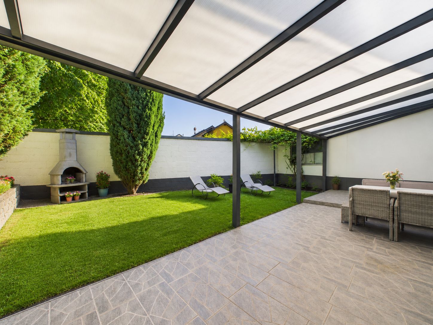 Überdachte Terrasse mit Esstisch, angrenzender Garten mit Liegen und Grillplatz.