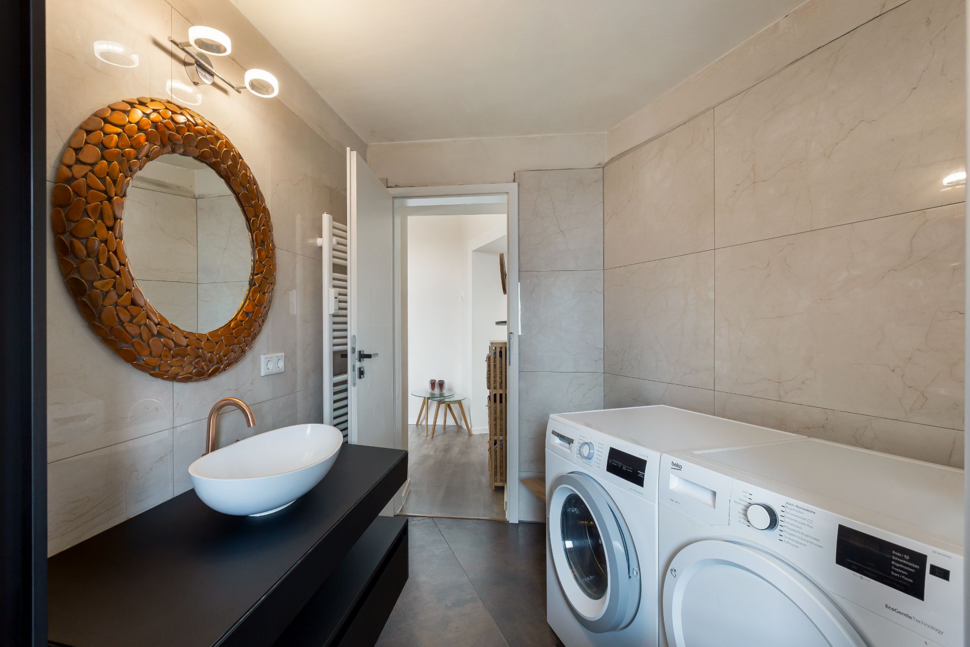 Modernes Badezimmer mit rundem Spiegel, Waschbecken, Waschmaschine und Trockner.