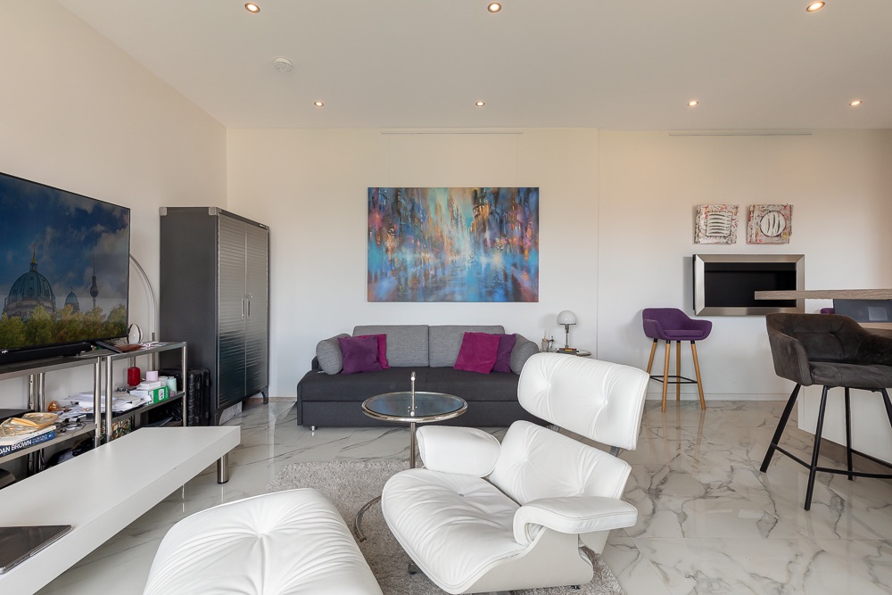 Modernes Wohnzimmer mit Fernseher, Sofa, Sessel und Marmorboden.
