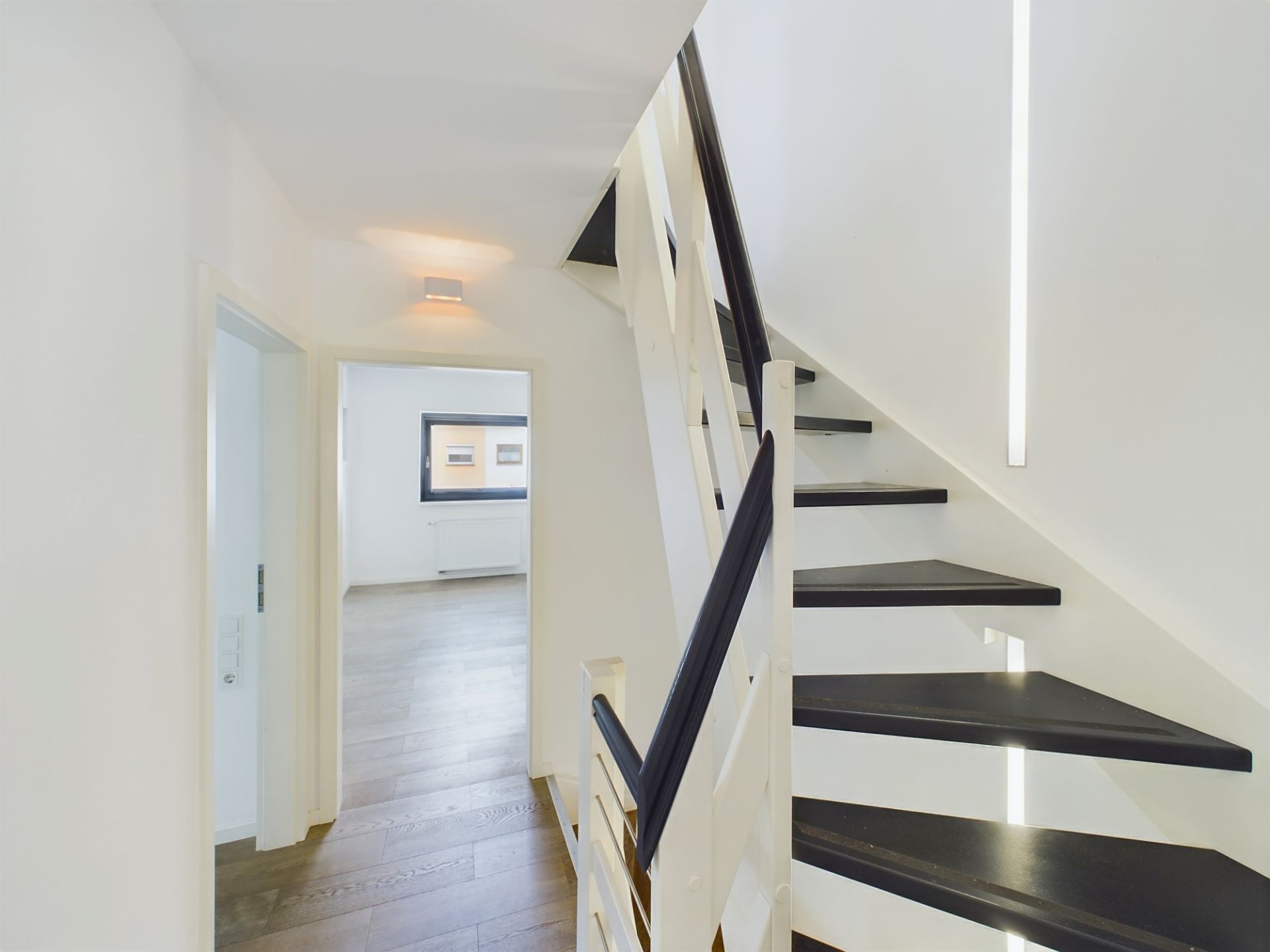 Moderne schwarze Treppe und Flur mit Holzboden, Blick in helles Zimmer mit Fenster.
