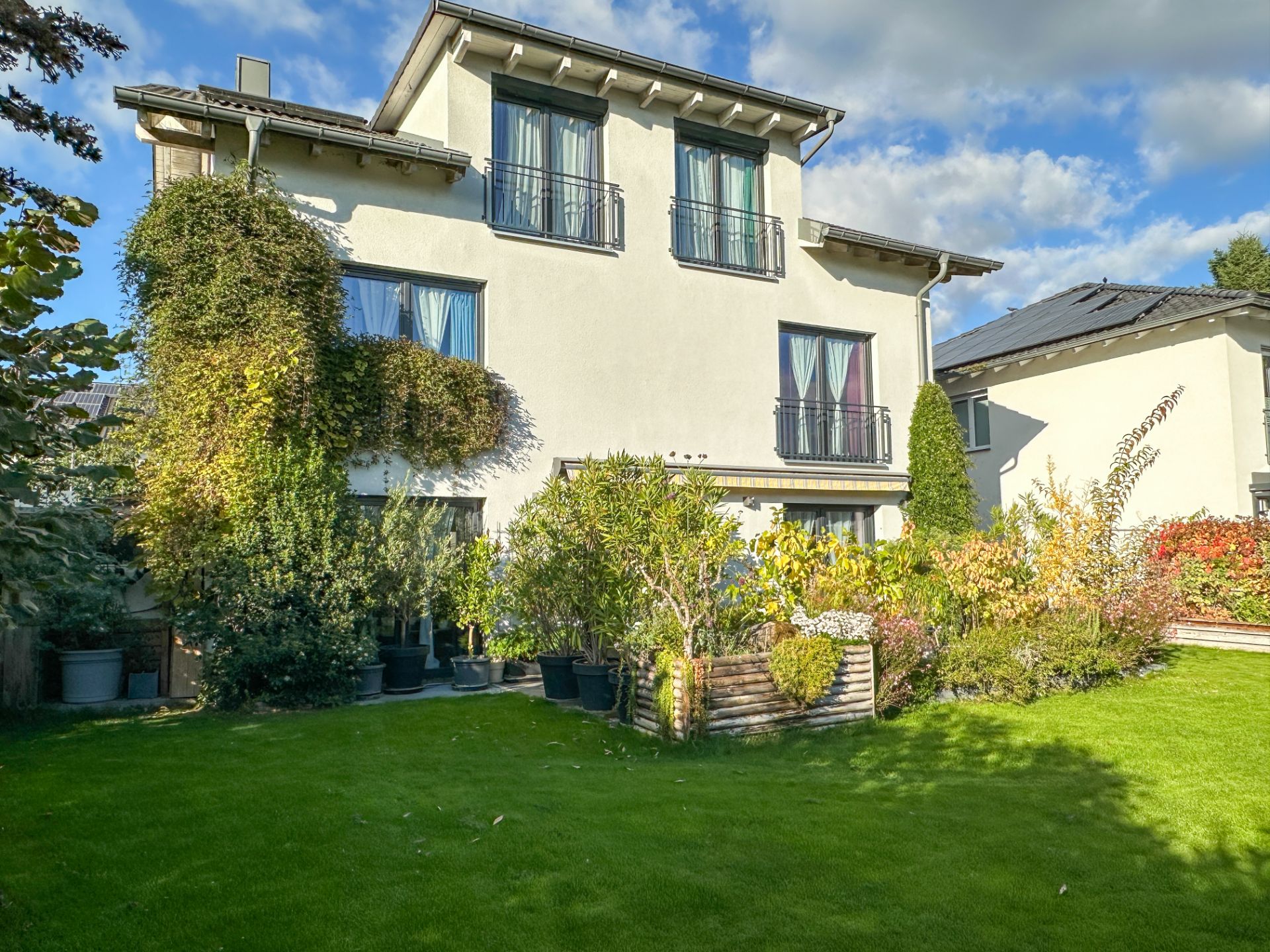 Zweistöckiges Wohnhaus mit Balkon, Garten und vielen Pflanzen vor dem Haus.