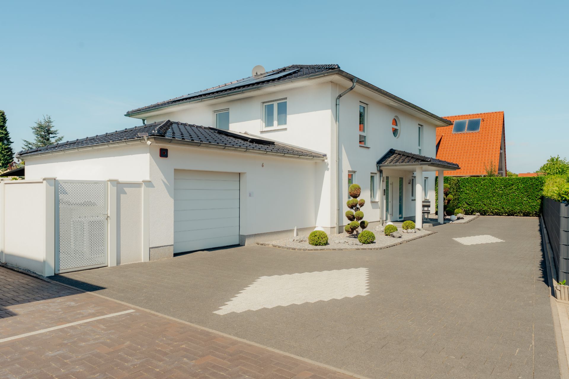 Modernes weißes Wohnhaus mit Garage, schwarzem Dach und gepflegtem Vorgarten.