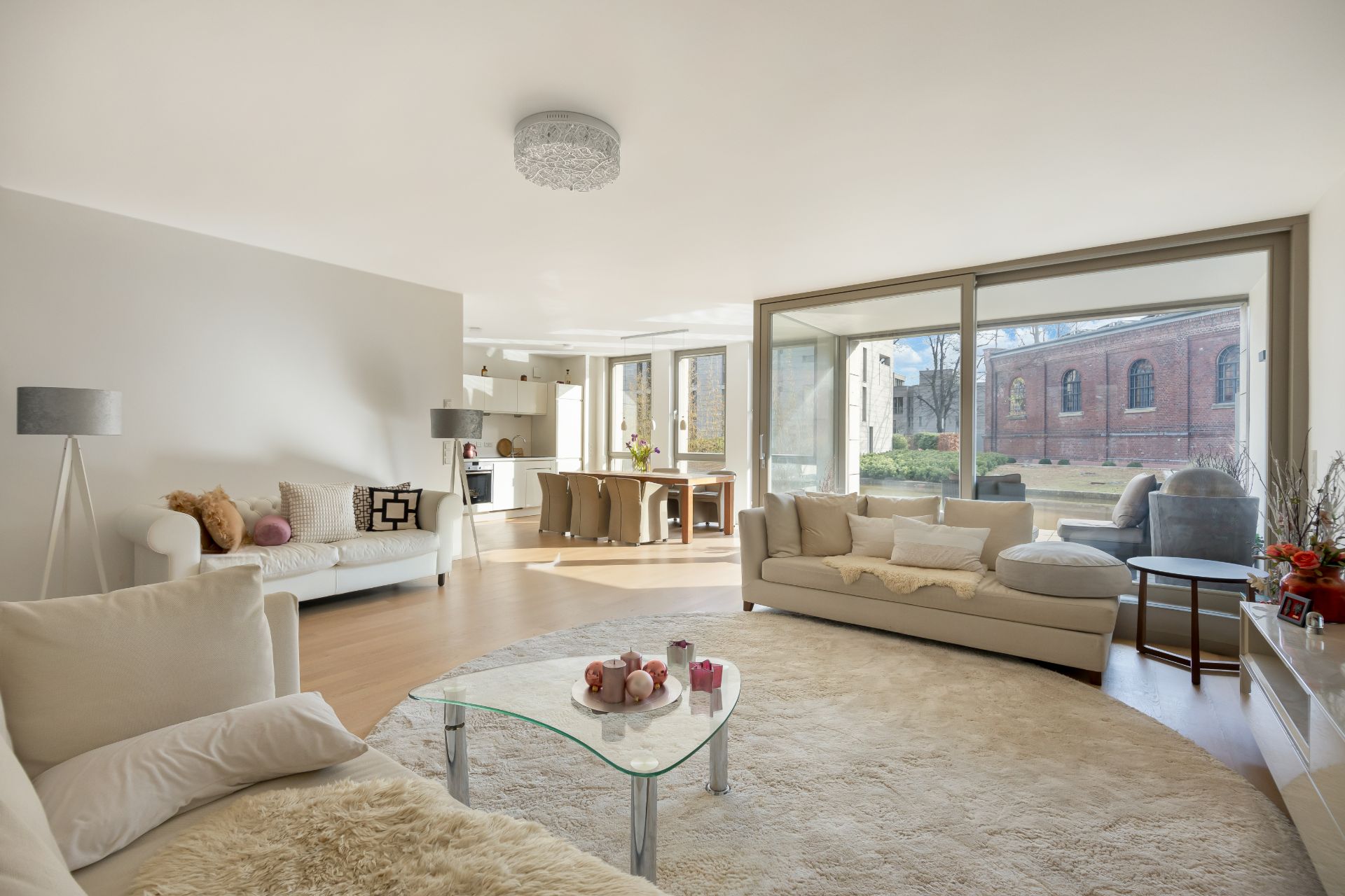 Helles Wohnzimmer mit großen Fenstern, hellen Sofas, Esstisch und Blick auf den Garten.