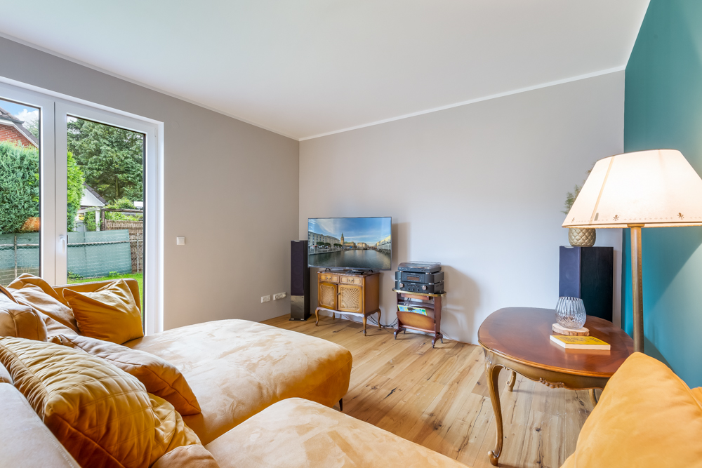 Helles Wohnzimmer mit gelbem Sofa, großem Fenster, Fernseher, Holztisch und Stehlampe.