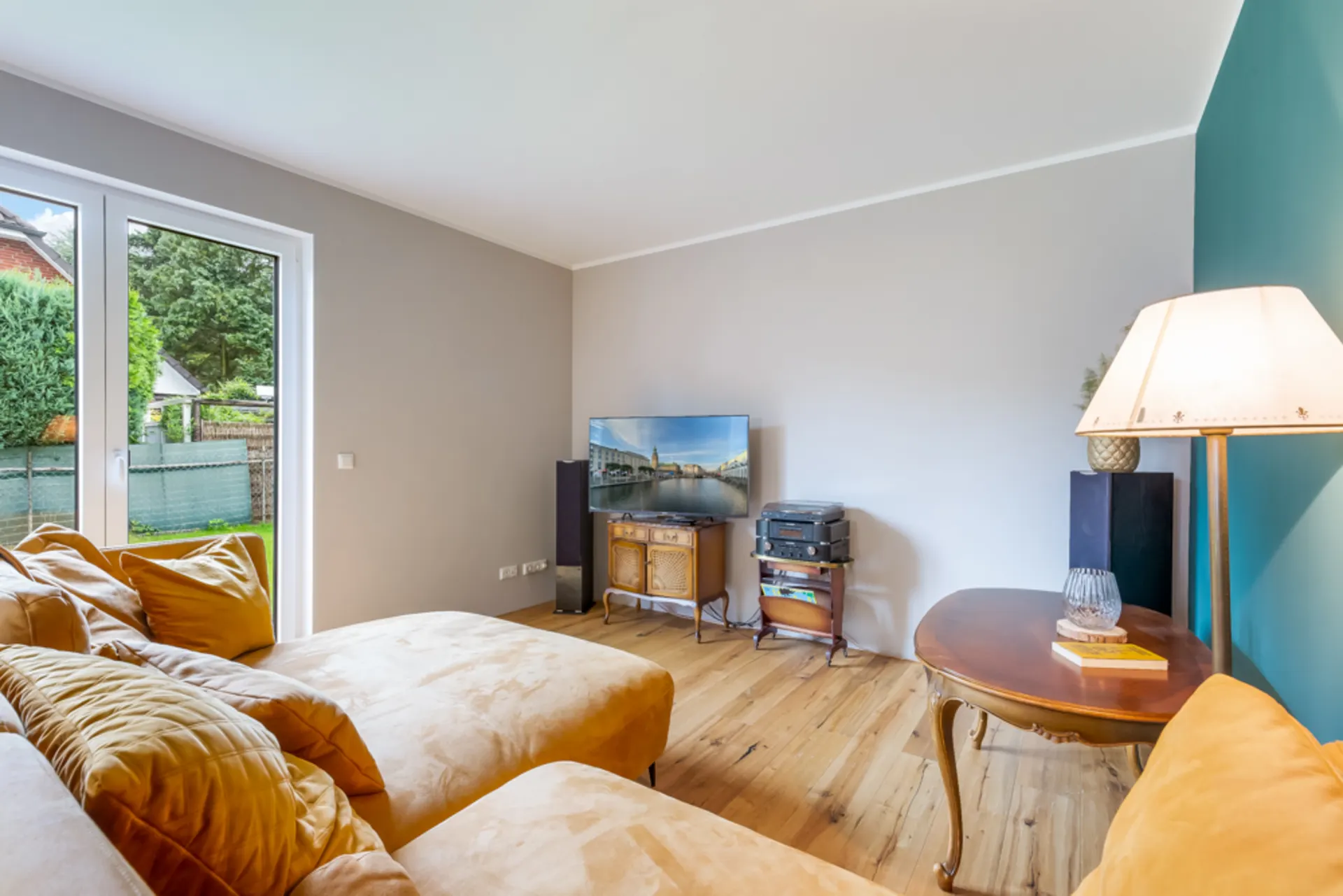 Helles Wohnzimmer mit gelbem Sofa, großem Fenster, Fernseher, Holztisch und Stehlampe.