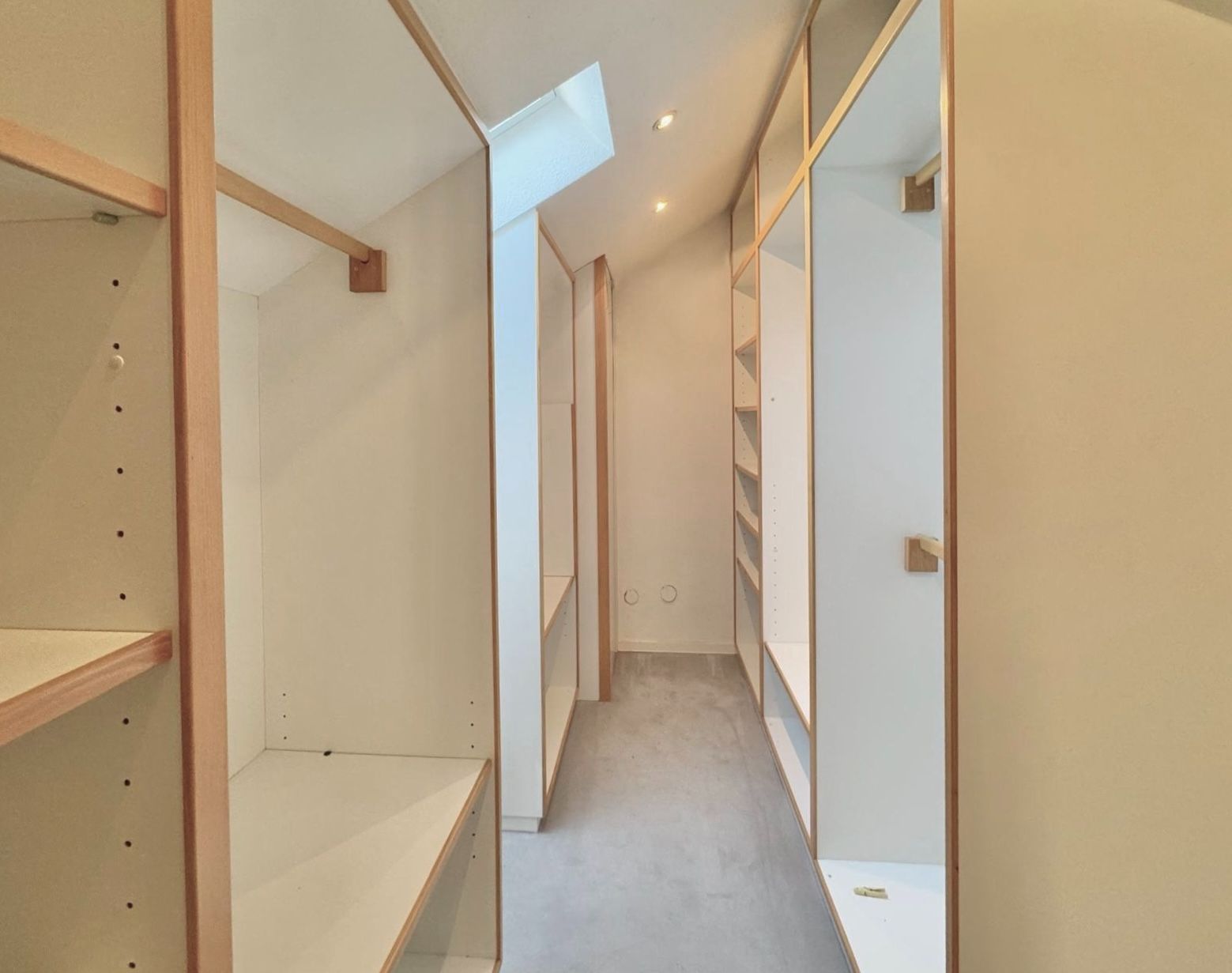 Schmaler begehbarer Kleiderschrank mit offenen Regalen und Kleiderstangen, Oberlicht an der Decke.