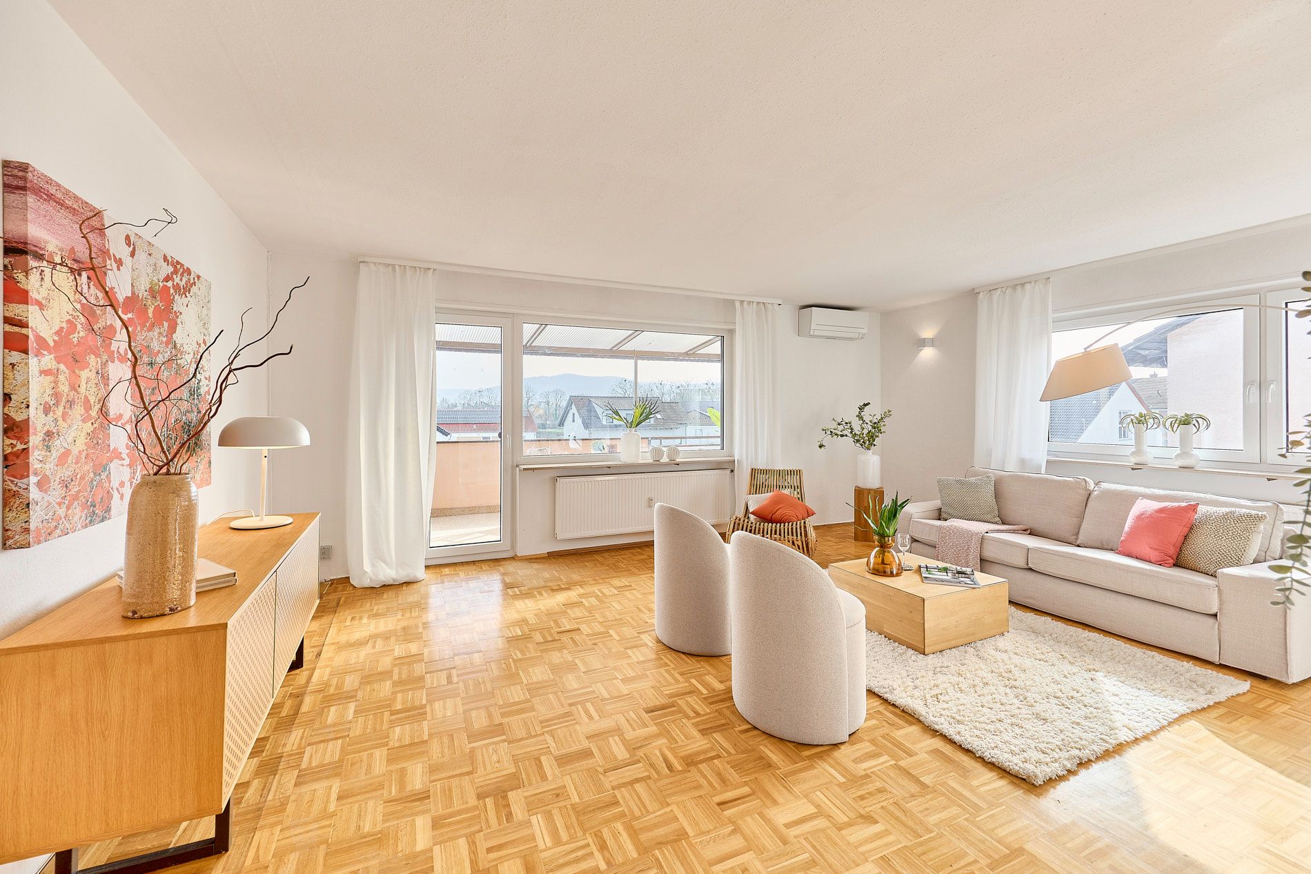 Helles Wohnzimmer mit Holzboden, Sofa, zwei Sesseln, Couchtisch und Zugang zum Balkon.