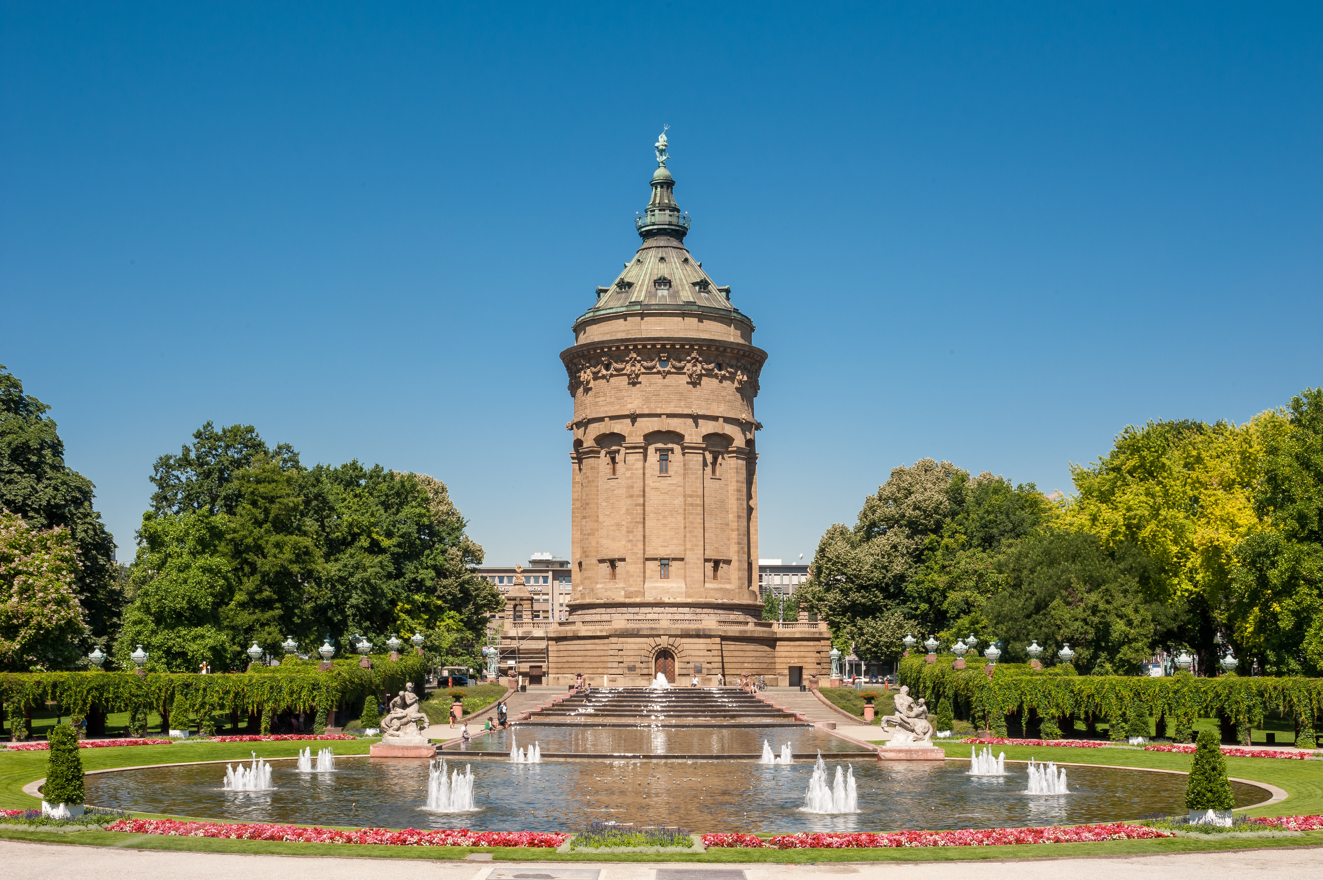 Ein großer, runder Turm vor einem Springbrunnen in einer grünen Parkanlage.