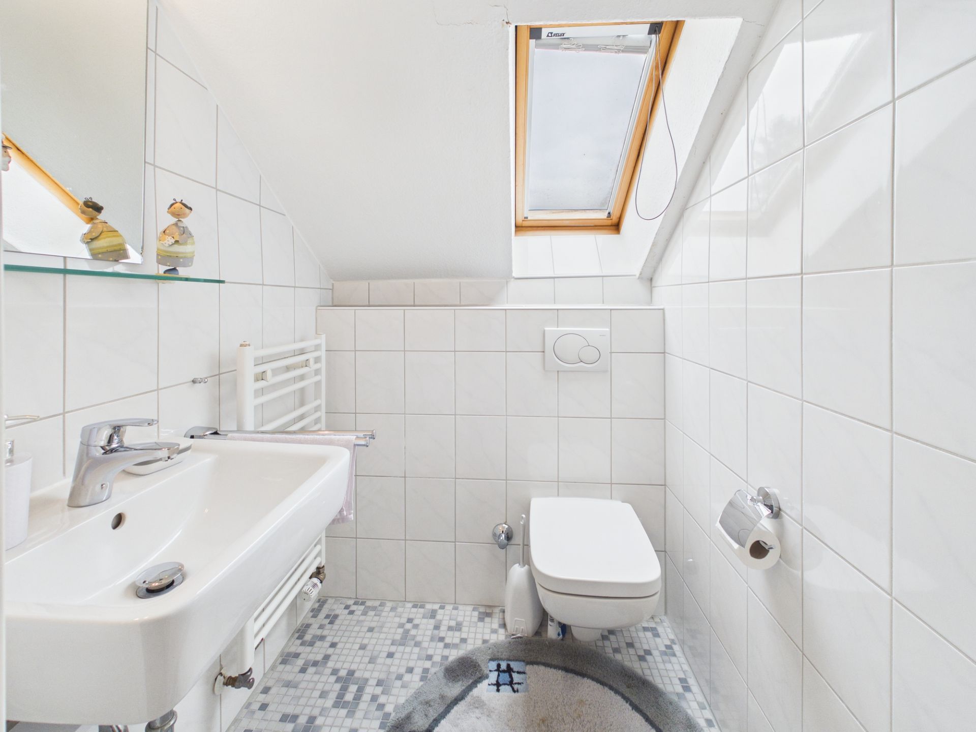 Kleines, weiß gefliestes Bad mit Waschbecken, WC und Dachfenster.