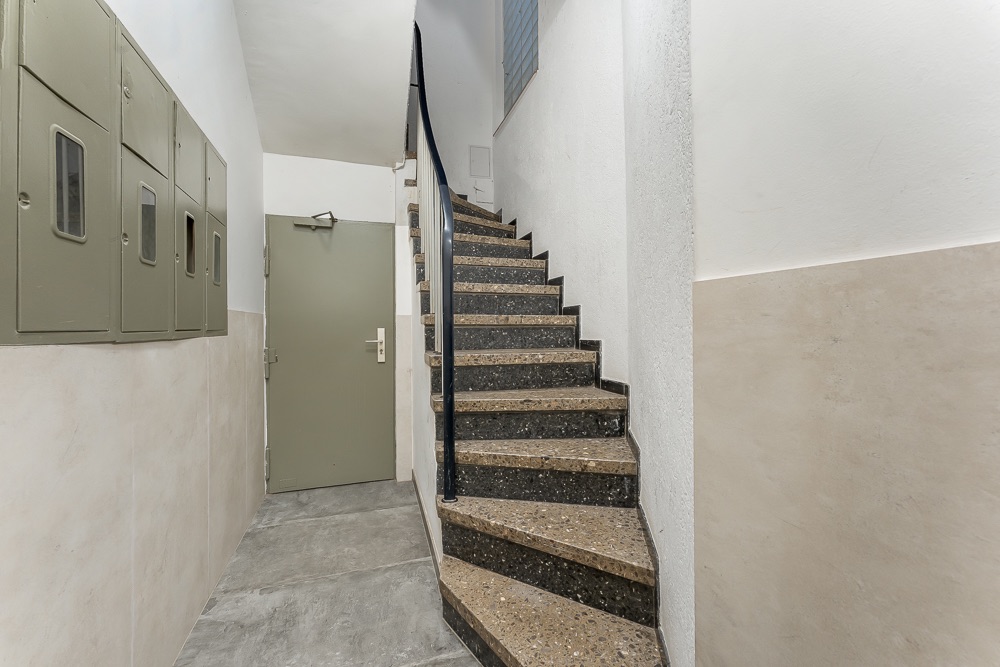 Treppenhaus mit brauner Treppe, Tür und grauen Verteilerkästen an der Wand.