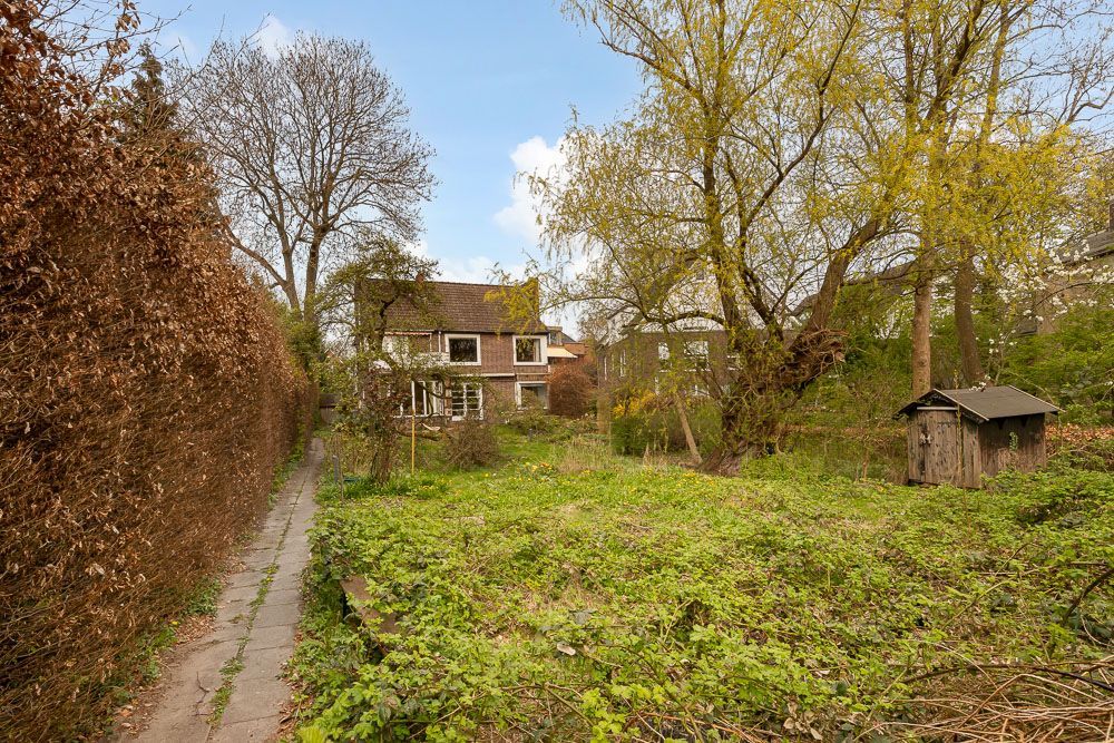 Großer Garten mit Weg, Baumhaus und Wohnhaus im Hintergrund.