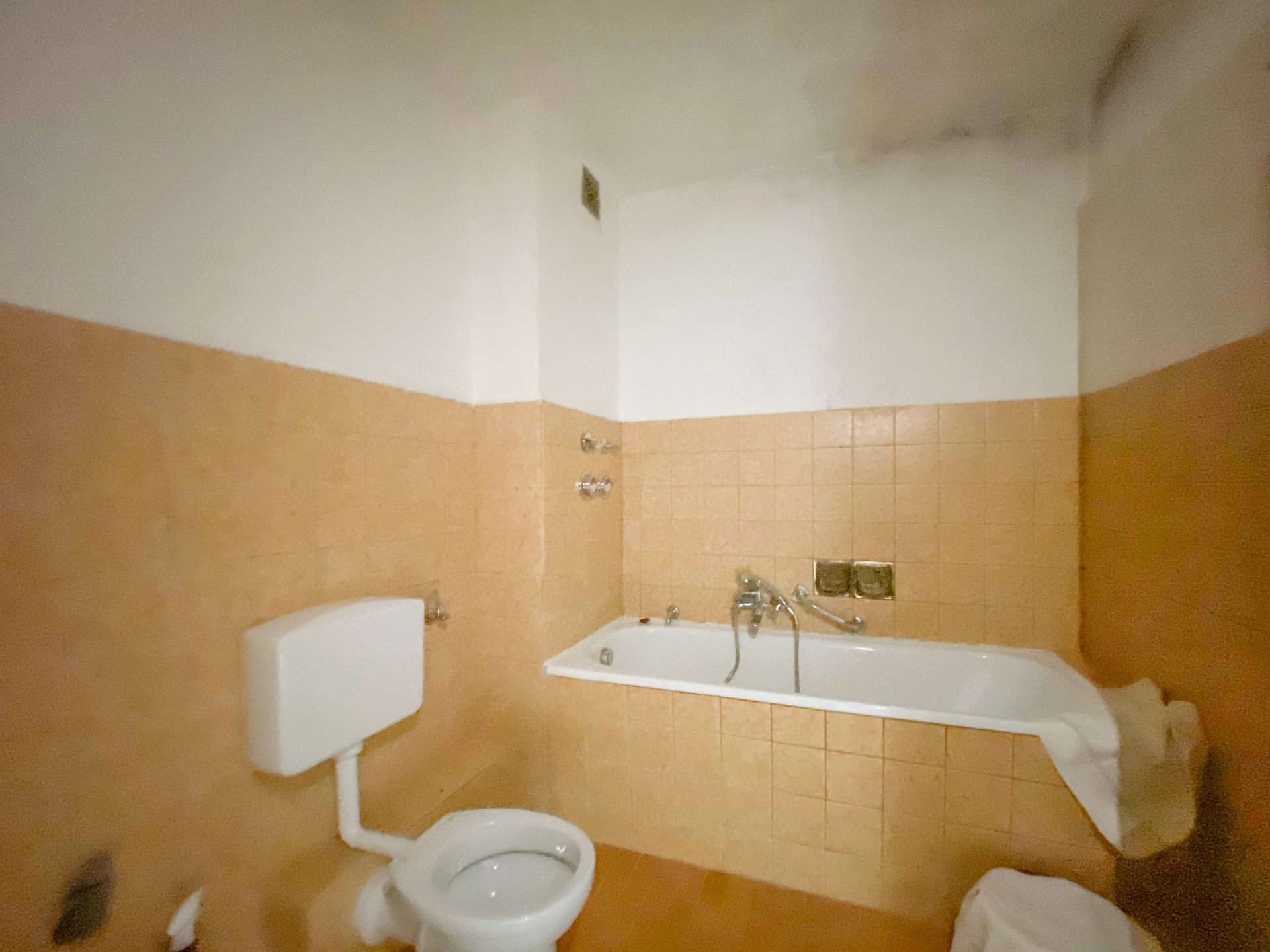 Badezimmer mit Badewanne, Toilette und beigefarbenen Fliesen an Wand und Boden.