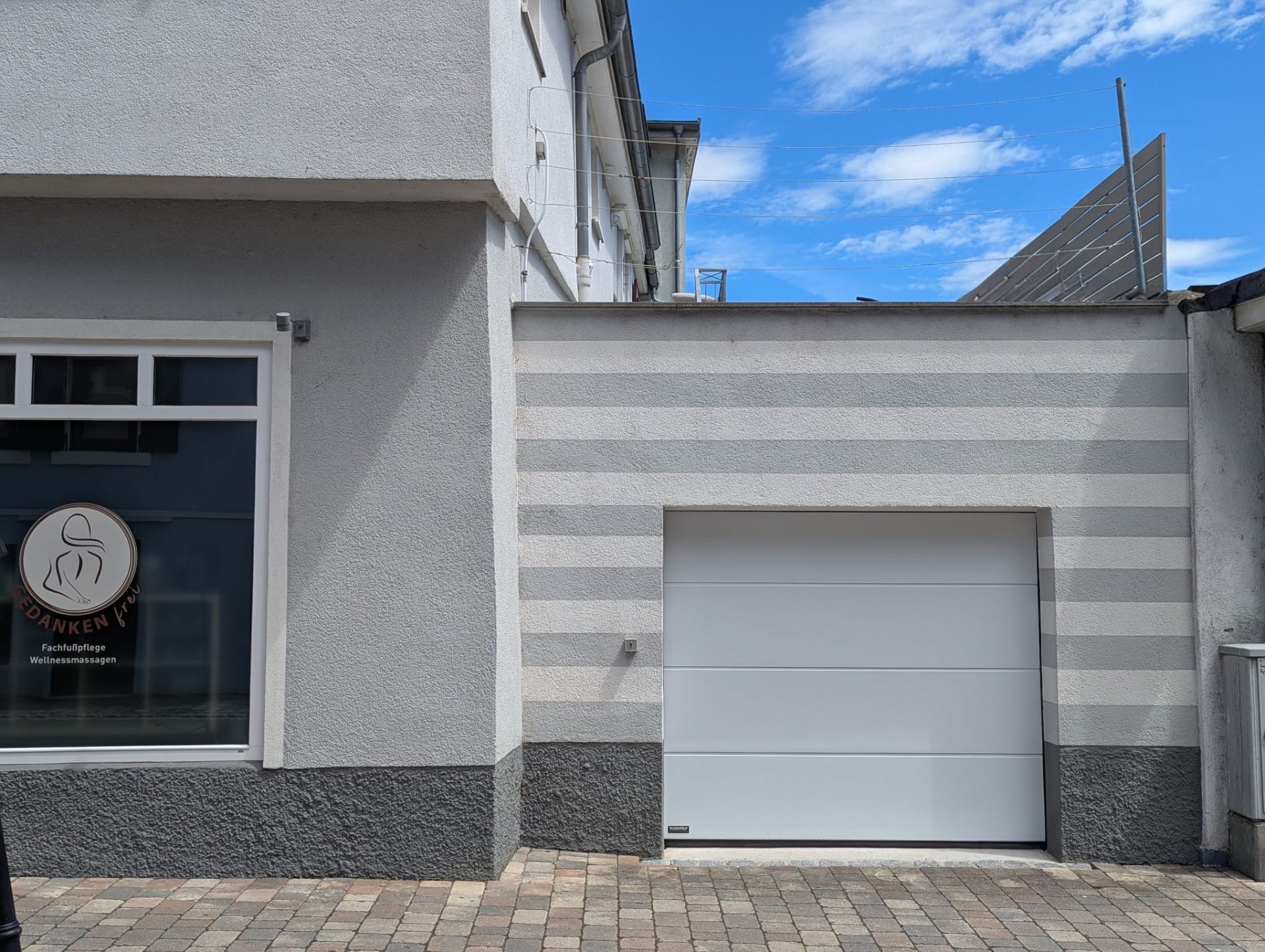 Helle Garage mit gestreifter Wand und angrenzendem Fenster, davor gepflasterter Boden.