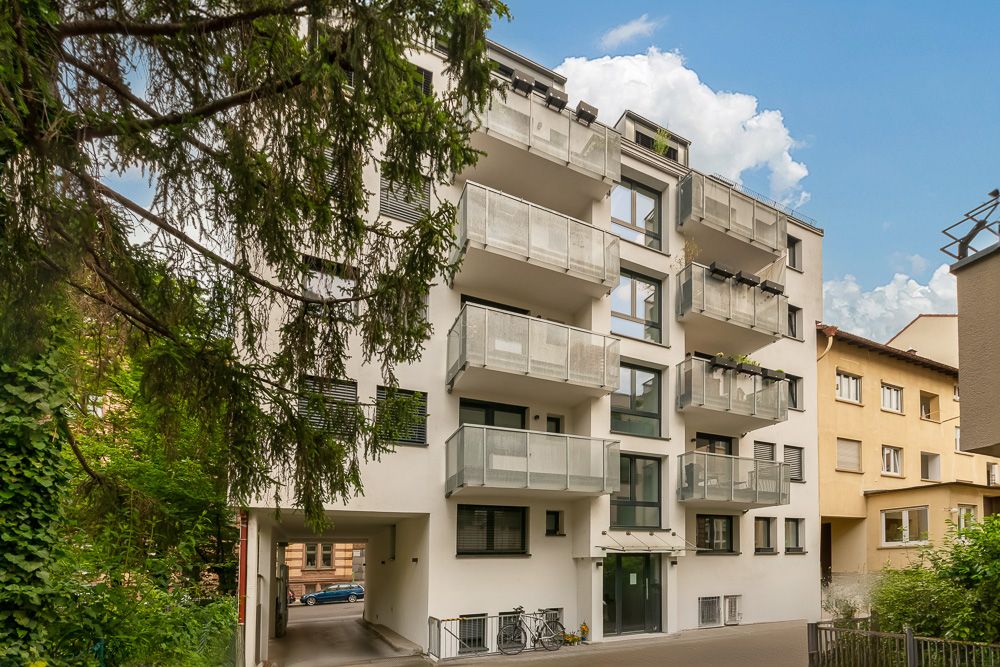 Modernes Wohnhaus mit mehreren Balkonen und Eingangsbereich, umgeben von Bäumen.